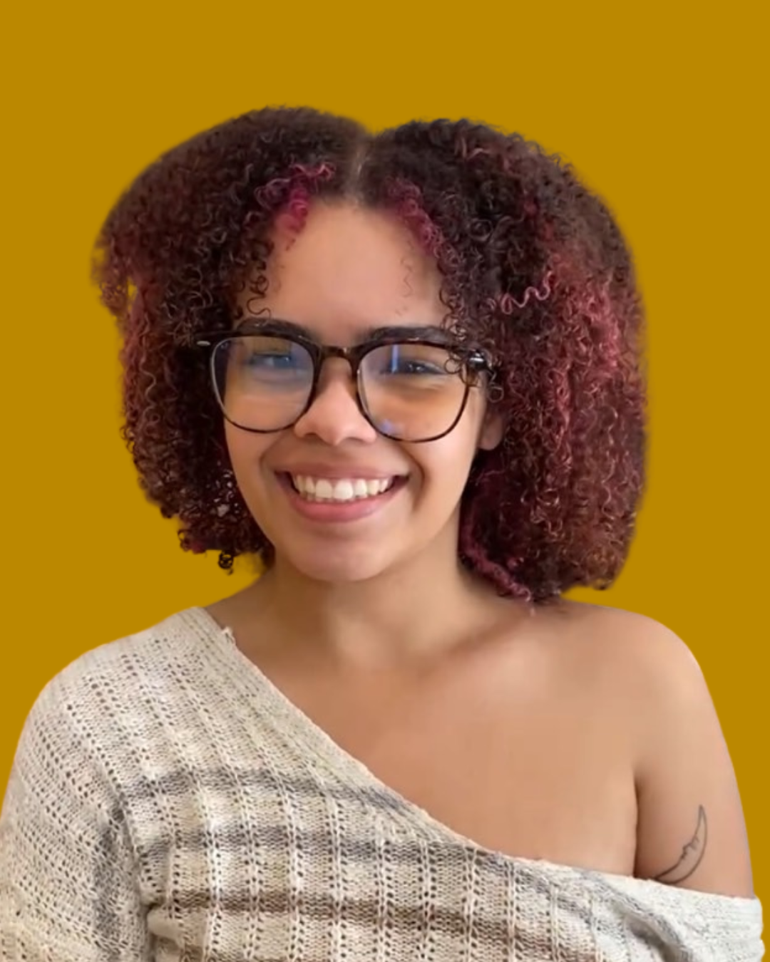 person with red and brown curly hair and brown glasses smiles at camera