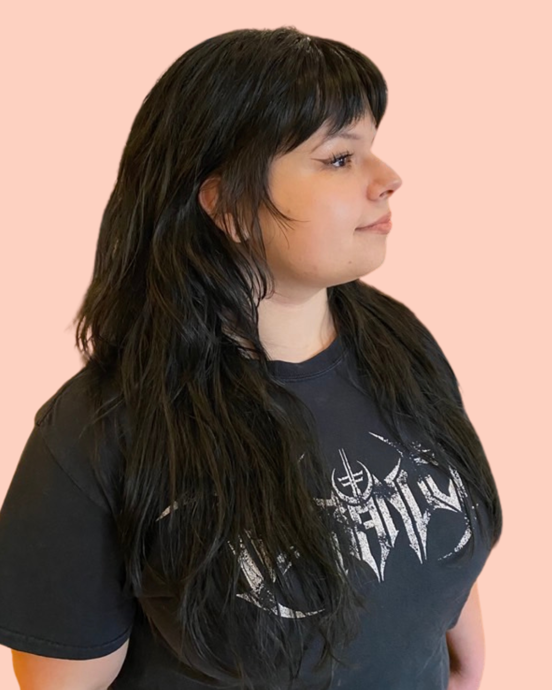 person with long black layered hair and bangs faces sideways in a black shirt
