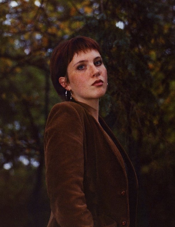 person with short hair standing outside in front of tree
