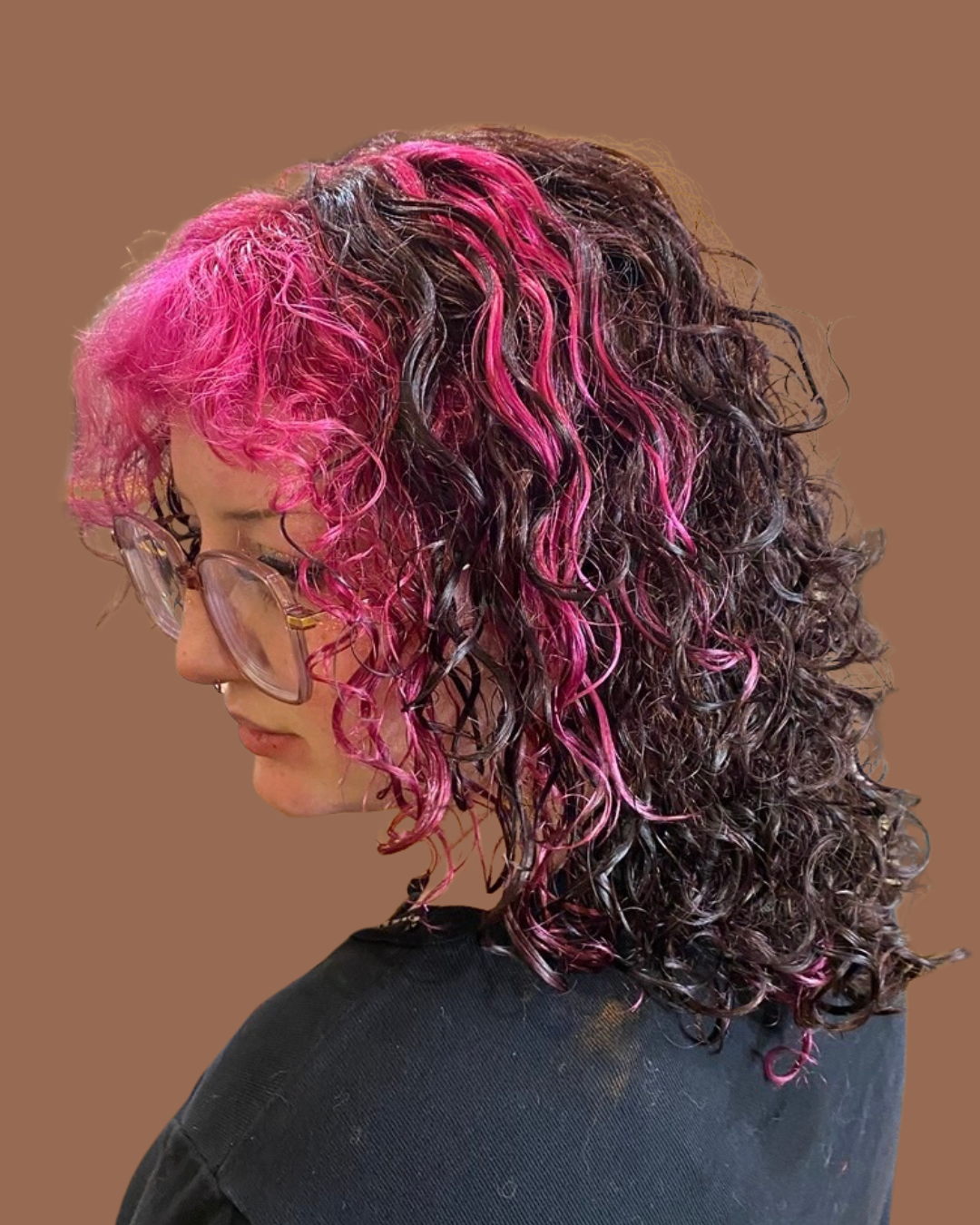 person with glasses who has light pink and dark purple and brown curly hair