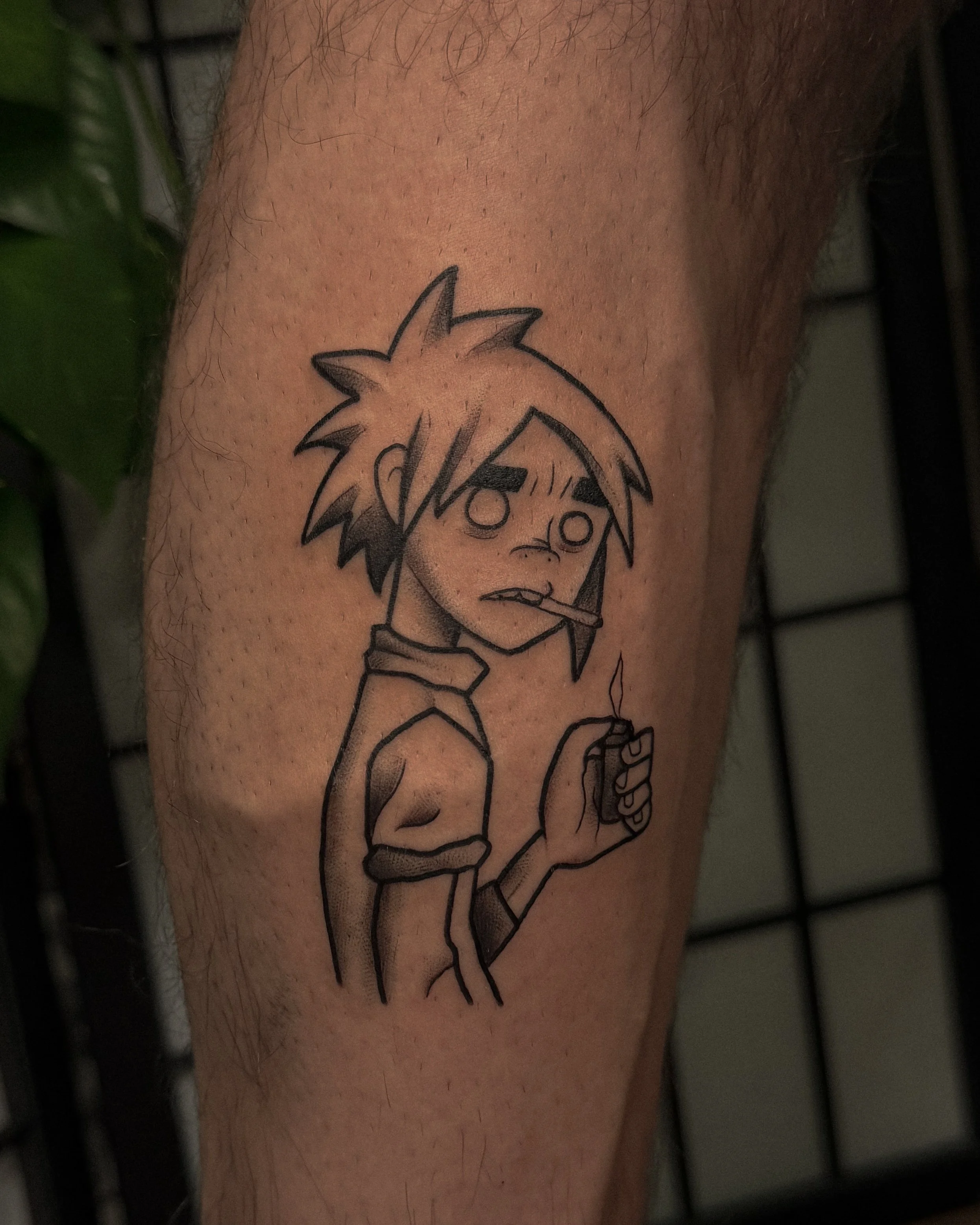 A tattoo of an anime-style character with spiky hair, big eyes, and a surprised expression, holding a cigarette in their mouth, located on a person's arm.