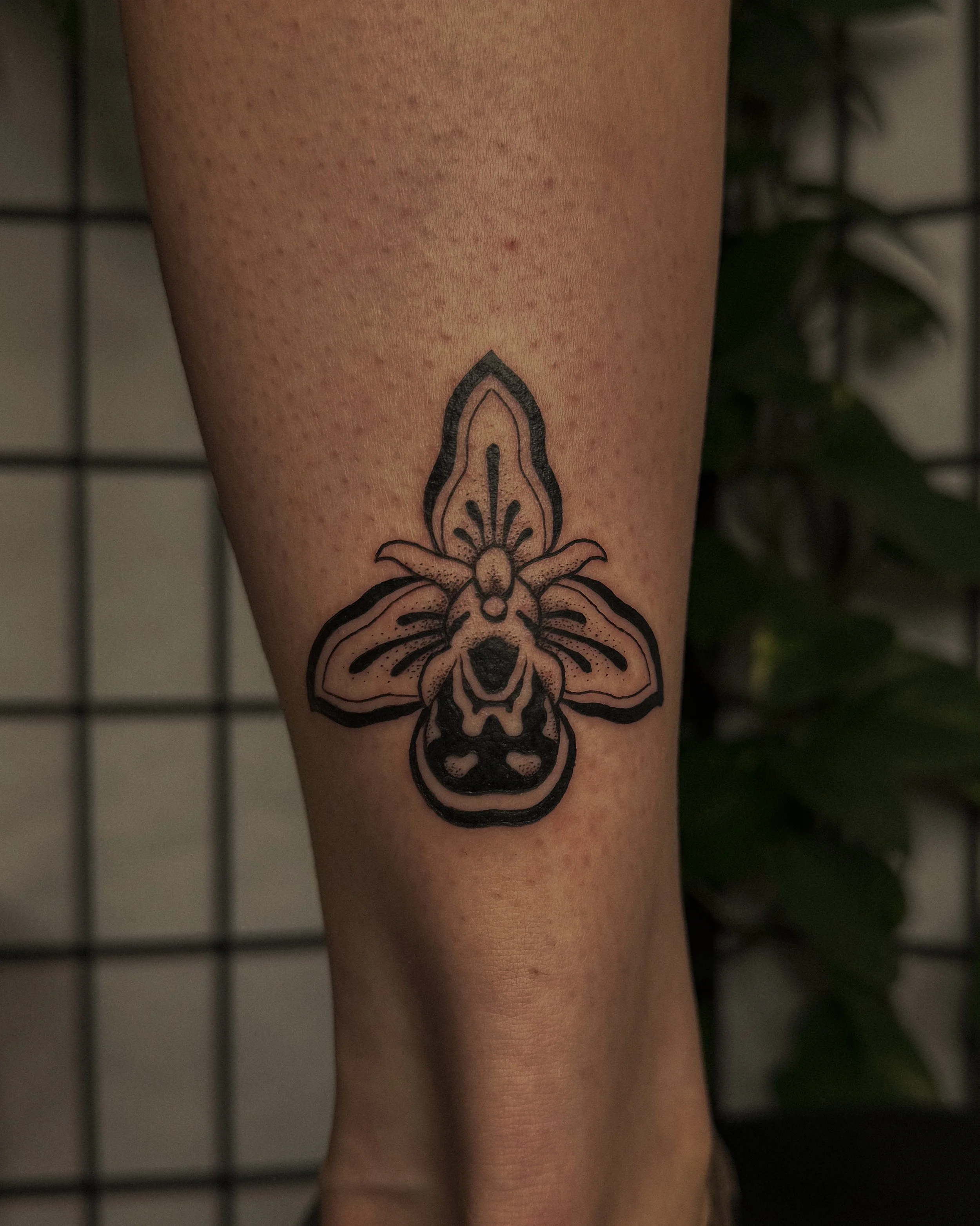 Close-up of a person's leg with a black outline tattoo of a bee and floral design.