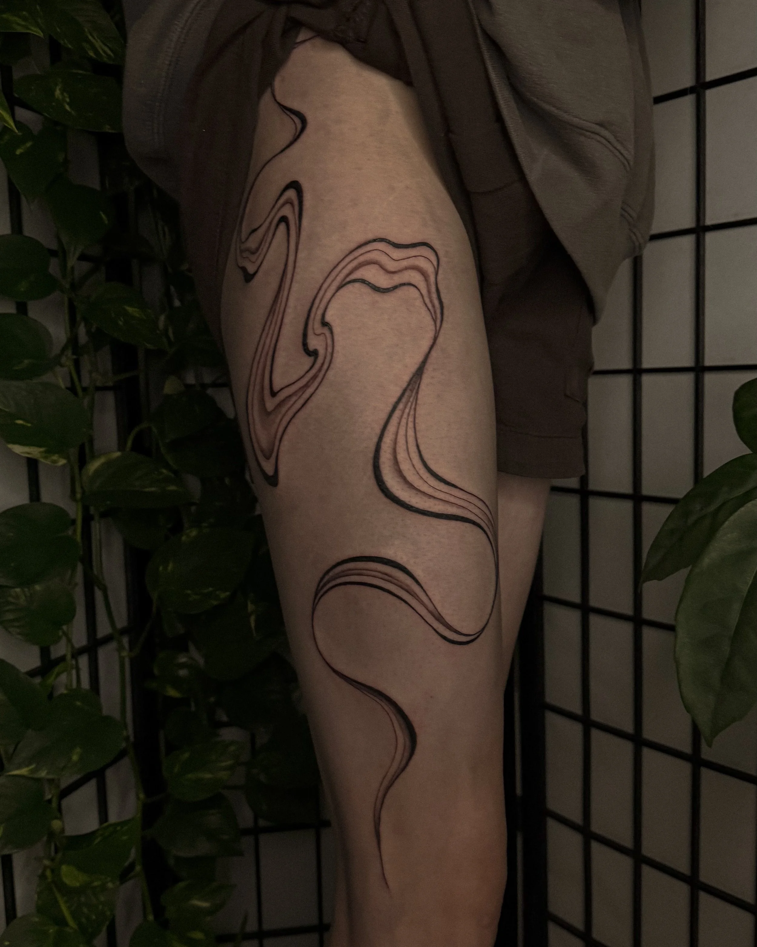 A person's upper thigh with a tattoo of abstract, flowing lines in black ink.