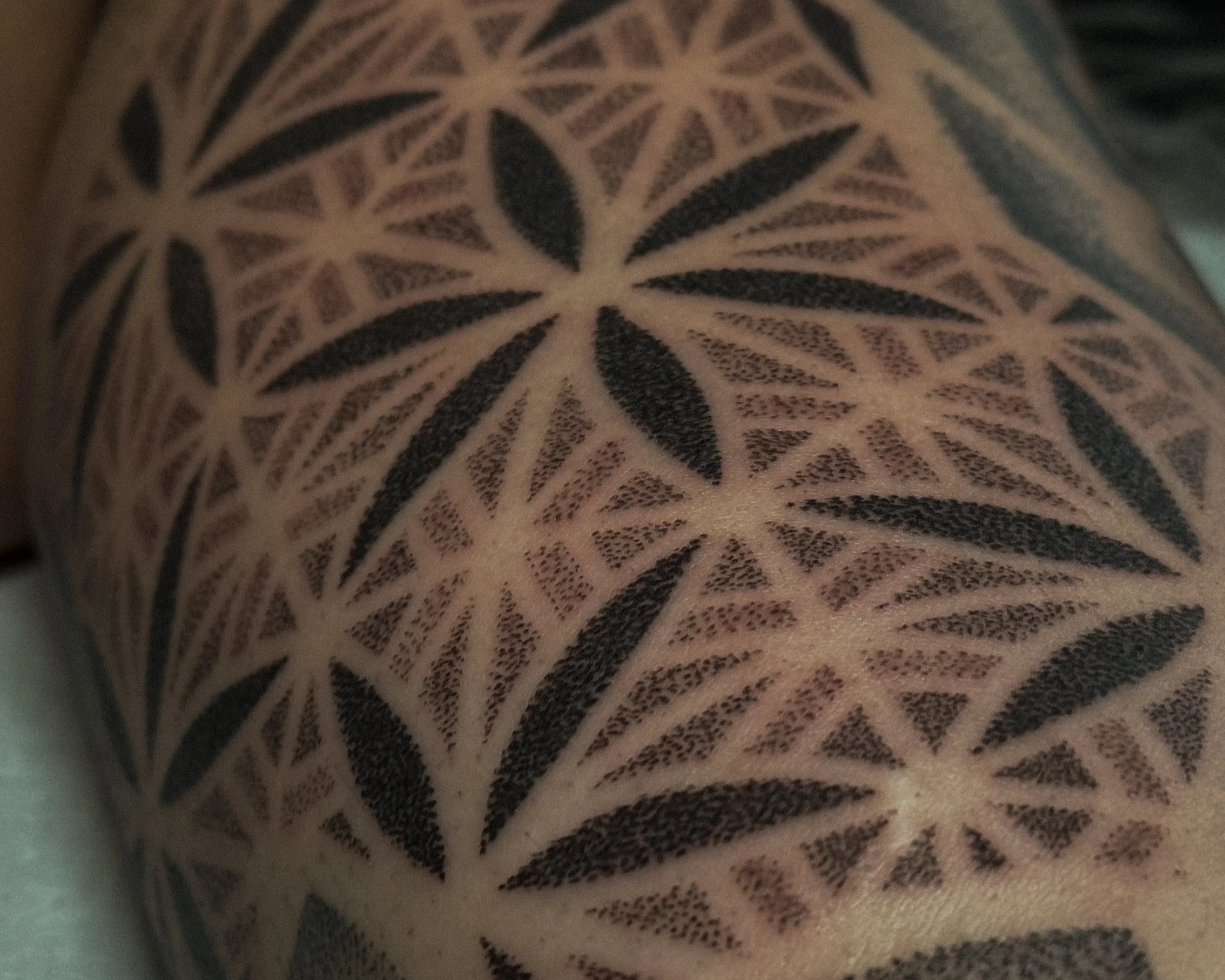Close-up of a tattoo featuring a geometric floral pattern with black ink on skin.