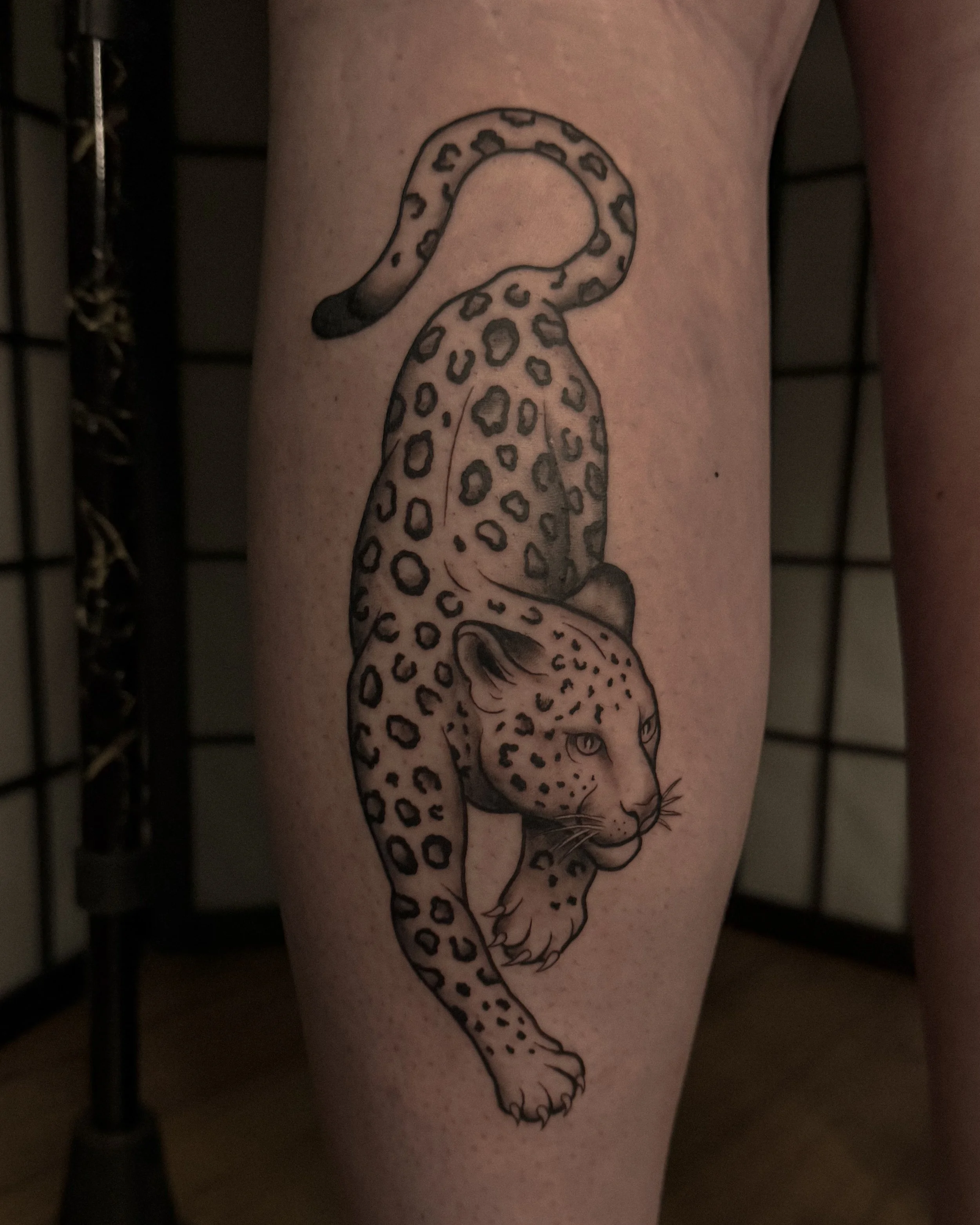A black outline tattoo of a leopard resting its head on its paw, with detailed spots and a calm expression.