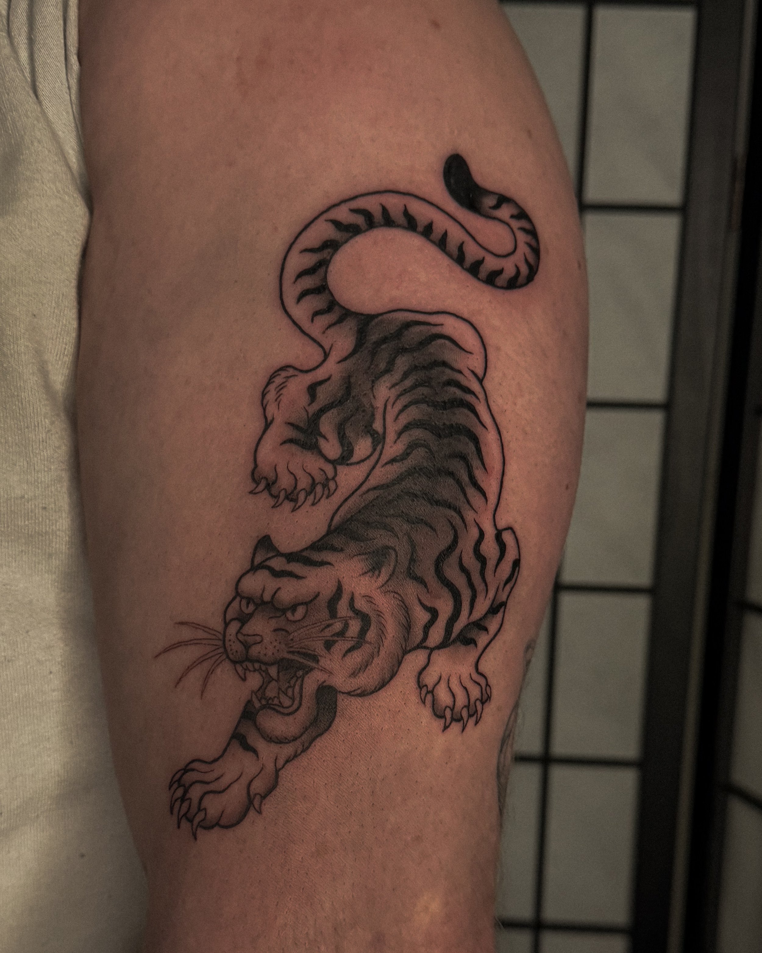 A black and white tattoo of a tiger on a person's upper arm.