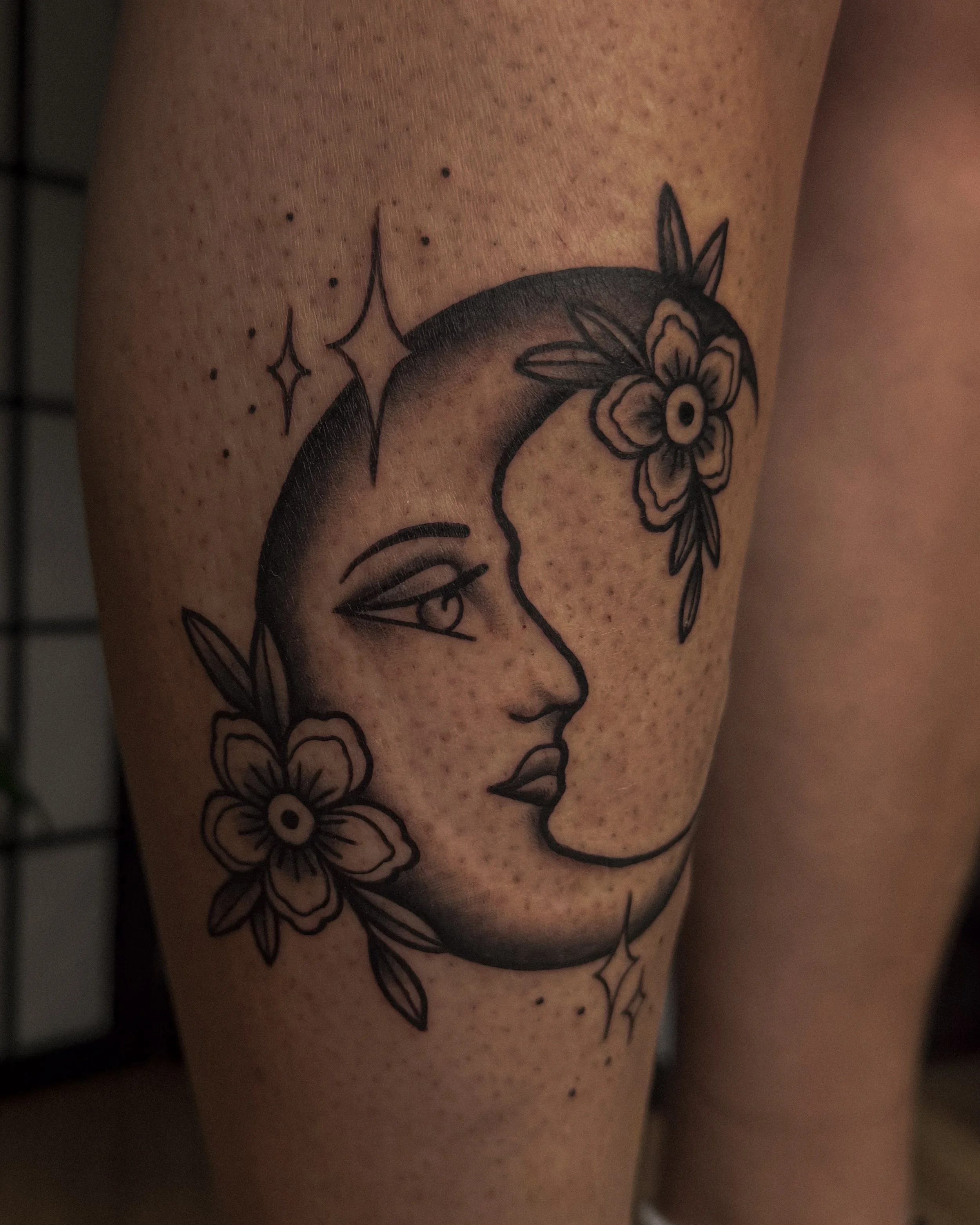 Close-up of a person's skin with a black tattoo outline of a unicorn's face, adorned with flowers, leaves, and stars.