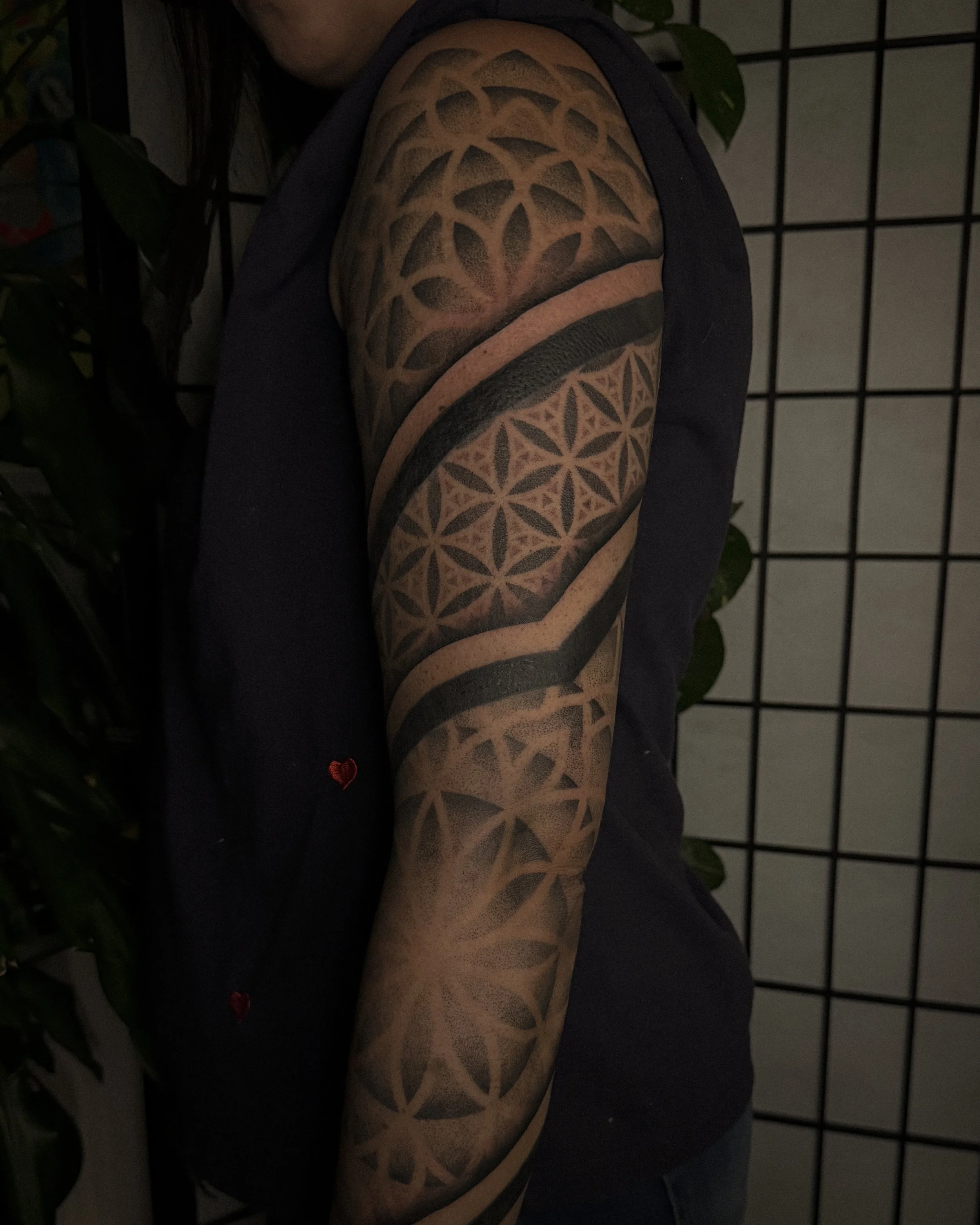 Close-up of a person's upper arm showing an intricate black geometric tattoo with repeating patterns and a solid black band near the shoulder.
