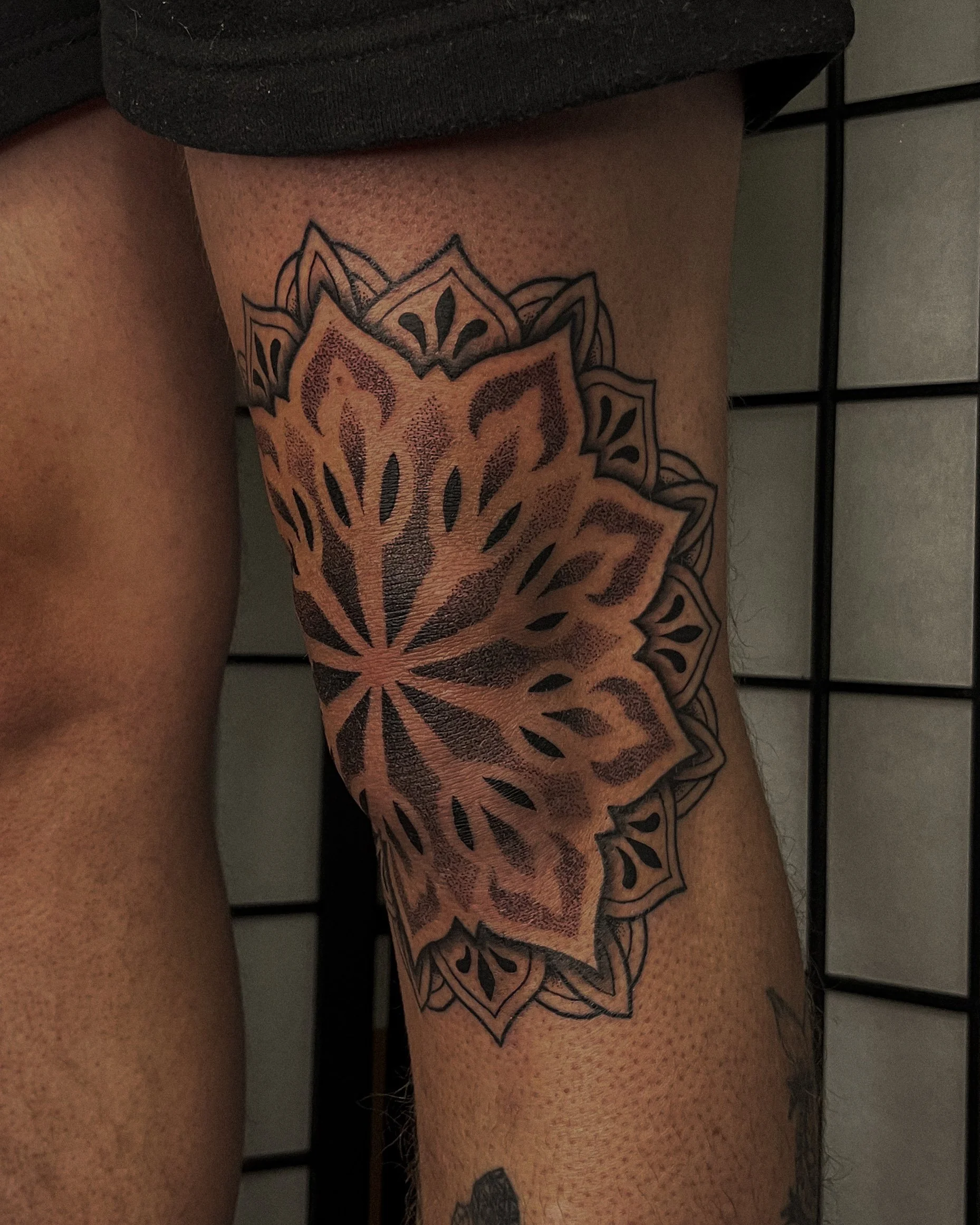 Tattoo of a mandala design on someone's thigh with a black grid background.