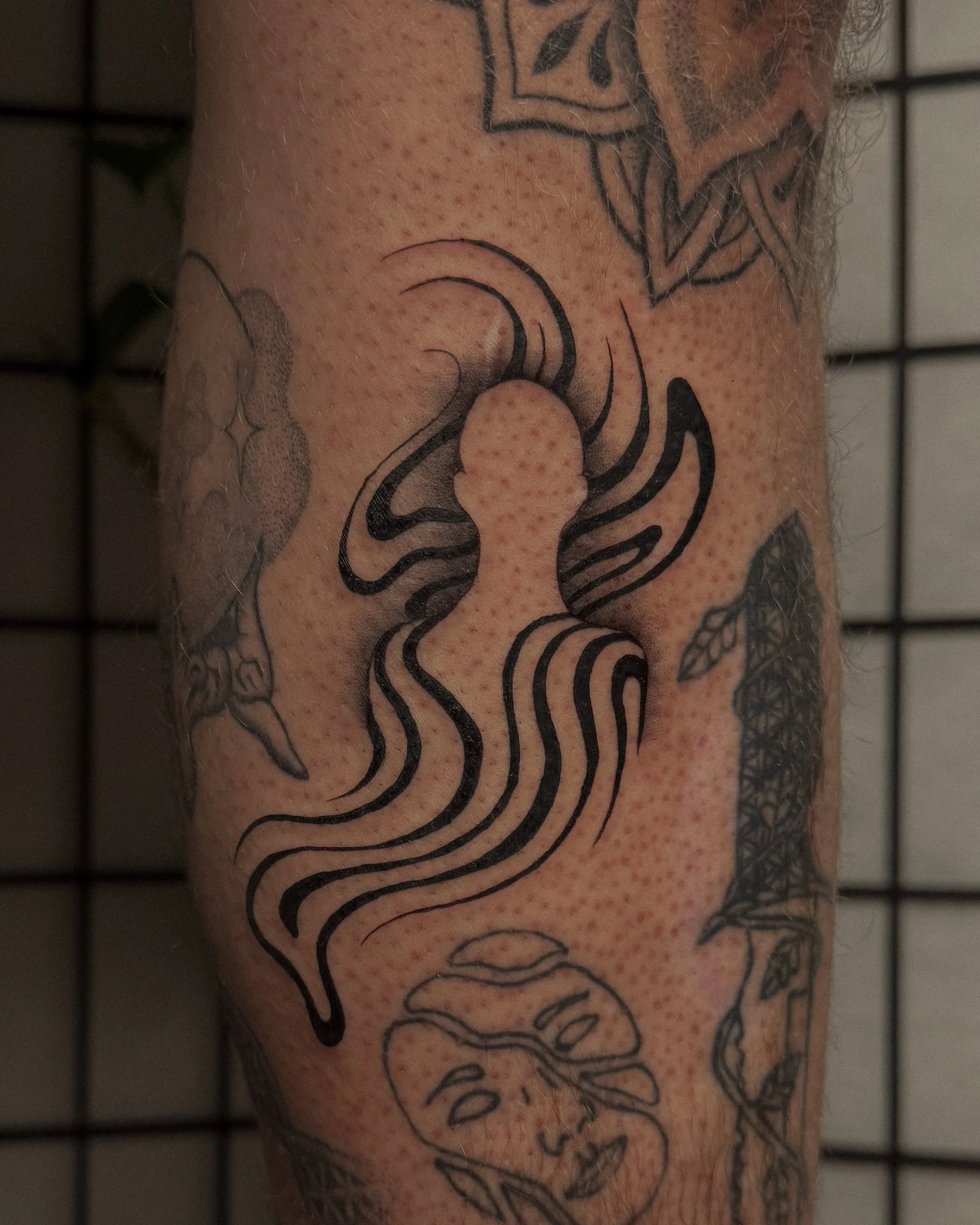 Close-up of a person's forearm with a black outline tattoo of a mermaid with long flowing hair and seashell details.