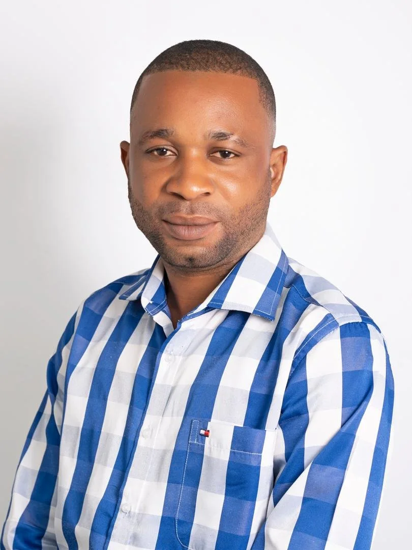 A man with short hair wearing a blue and white checkered shirt, posing against a plain white background.