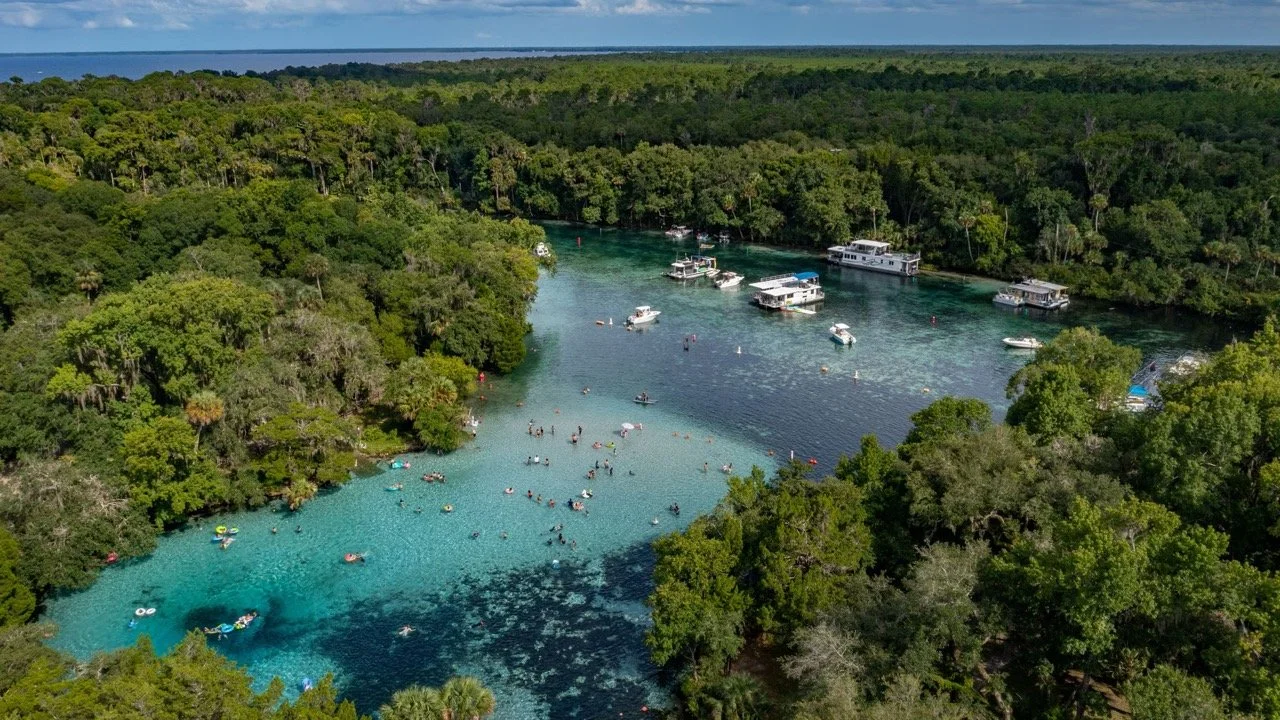 Kayakers and boats on crystal-clear water surrounded by forest in Ocala National Forest.