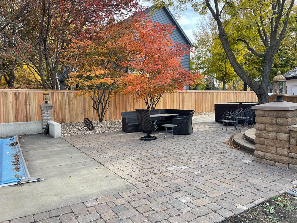 A backyard patio with a wooden fence, trees with fall foliage, outdoor seating including a corner sofa. Great Plains Fence is an expert fence installation and repair company in Sioux Falls, South Dakota.