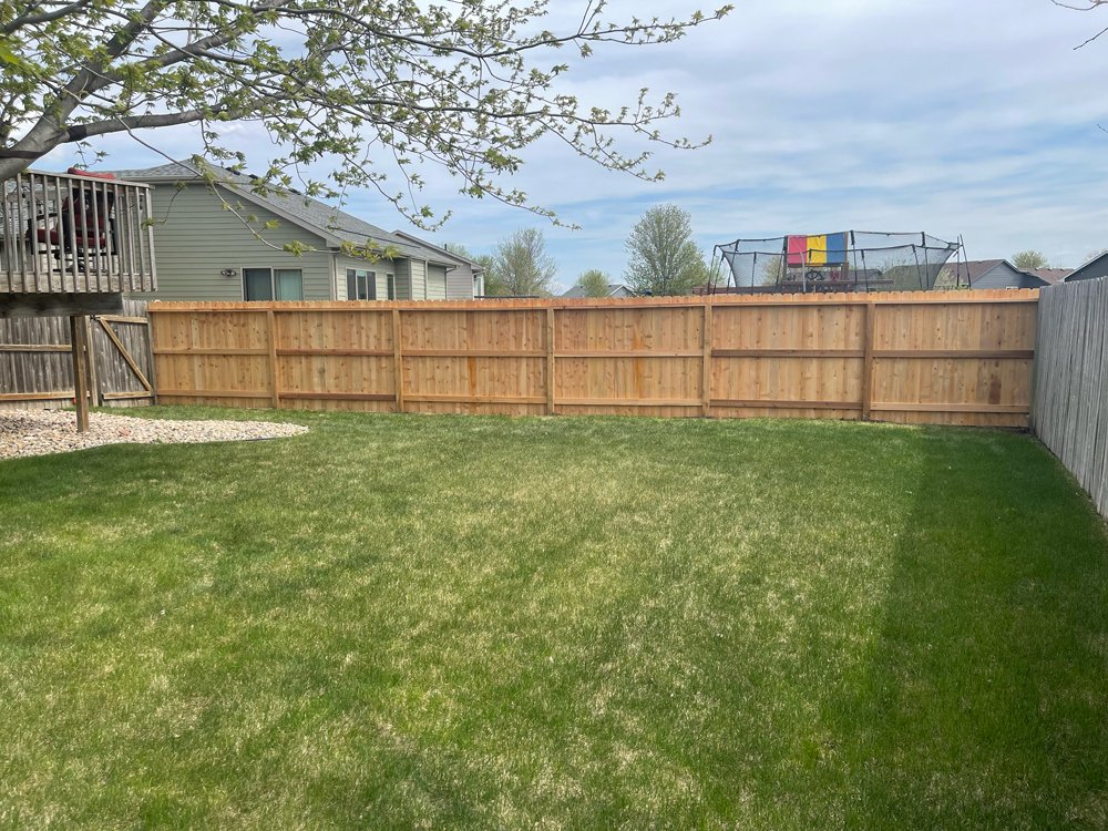 A backyard with green grass, wood privacy fencing, and a trampoline with a colorful shade in the background. Great Plains Fence is an expert fence installation and repair company in Sioux Falls, South Dakota.