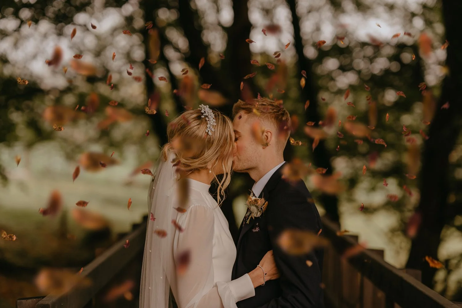 Autumn wedding couple kissing under falling leaves