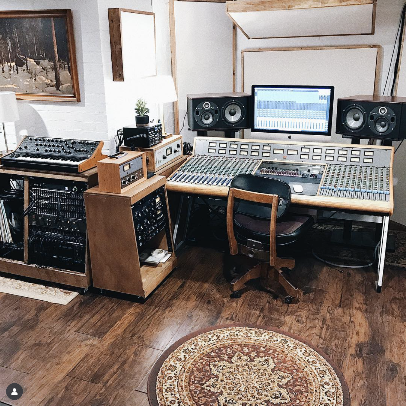 Recording studio with mixing console, speakers, computer, and musical instruments.
