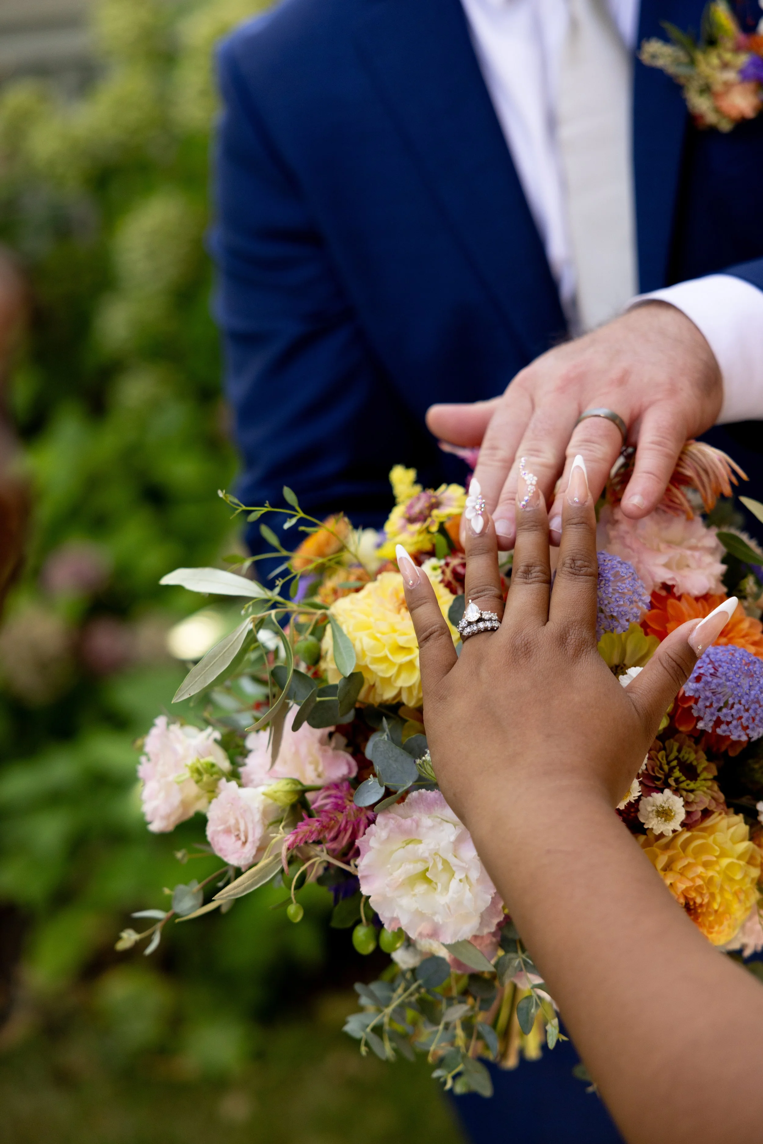 Bride and groom showing their wedding rings over a colorful seasonal bouquet designed with locally grown flowers grown and designed by Moonlight Blooms Farm.