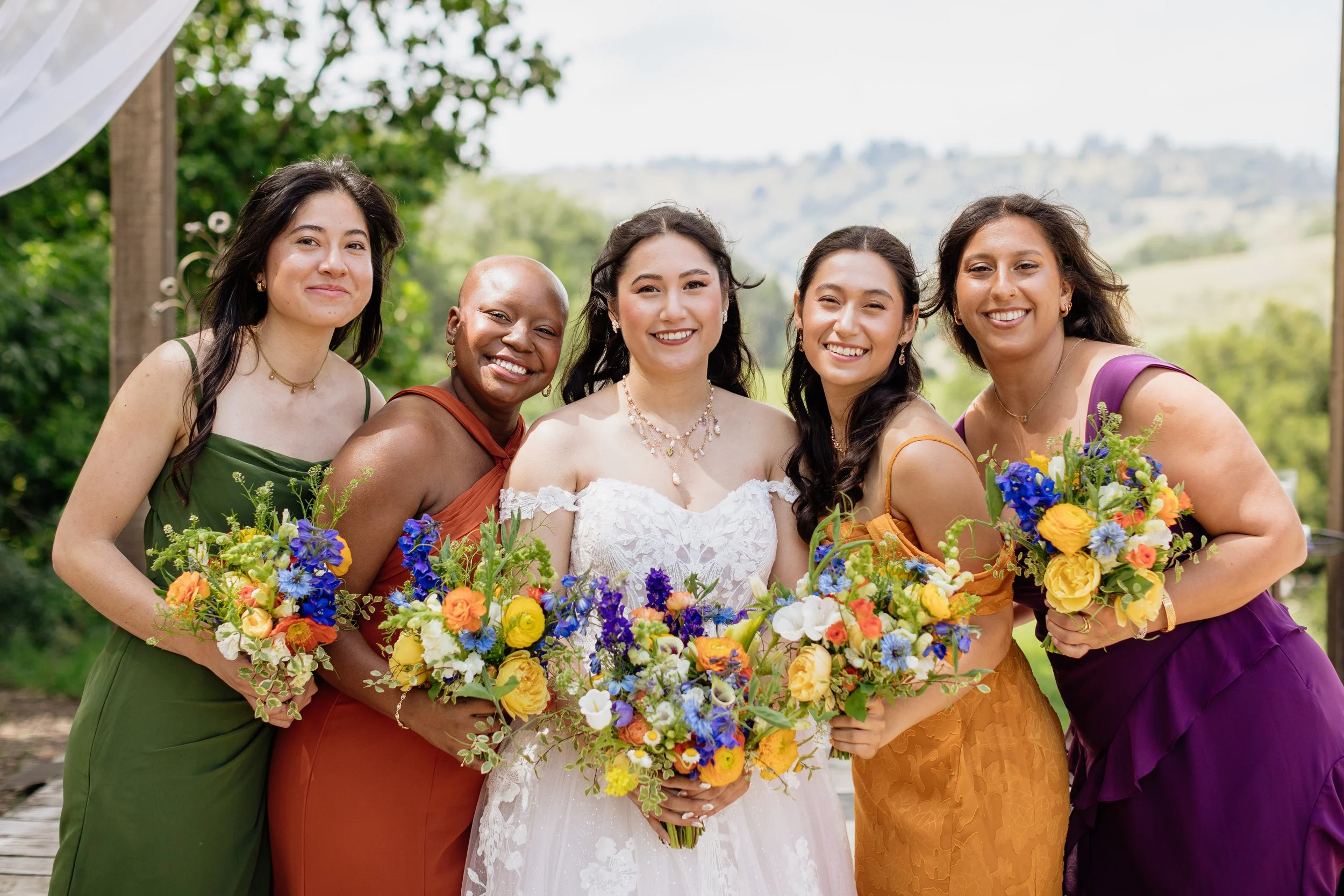 Bride and bridesmaids holding colorful seasonal bouquets at a Sonoma County wedding. Garden inspired bouquets featuring locally grown flowers in shades of blue, yellow, orange and white.