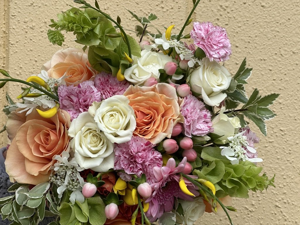 Colorful flower bouquet with roses and carnations against a textured wall.