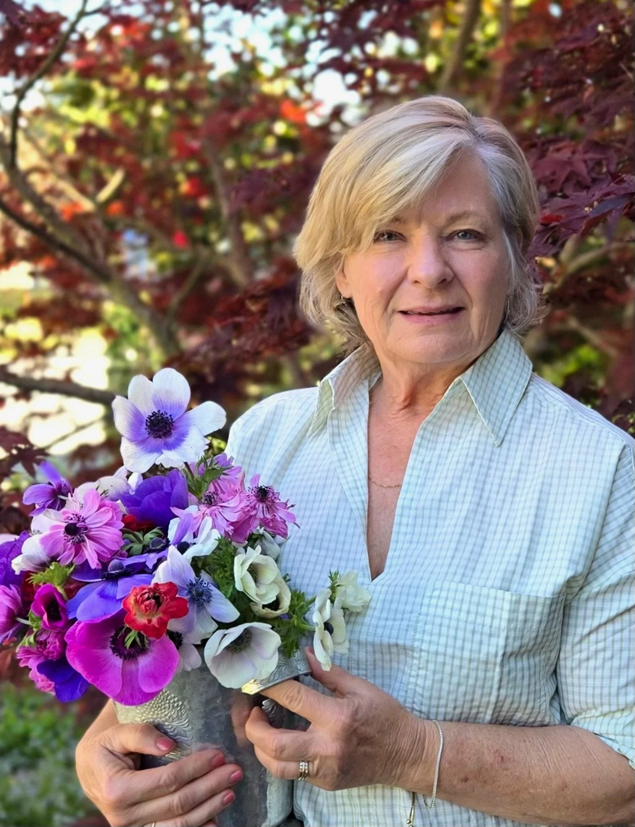 Woman holding a bouquet of colorful flowers with a blurred background of autumn trees.