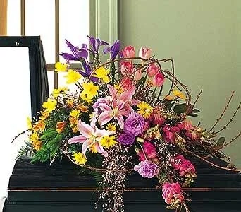 A floral arrangement with pink lilies, purple and yellow flowers, and greenery on top of a black piano.