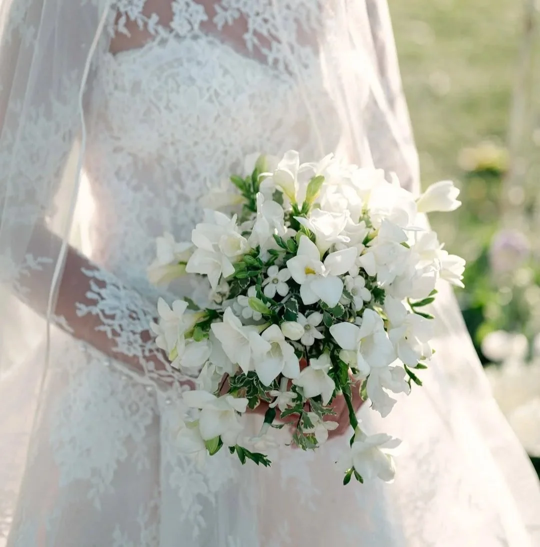 Bride holding a white flower bouquet while wearing a lace wedding dress and veil.