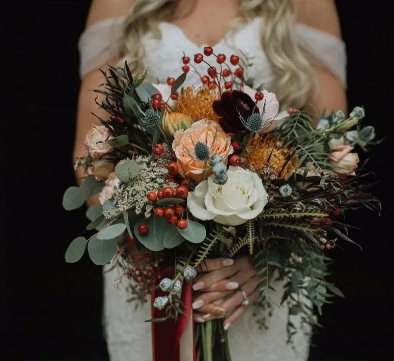Woman holding a large bouquet of colorful flowers and greenery.