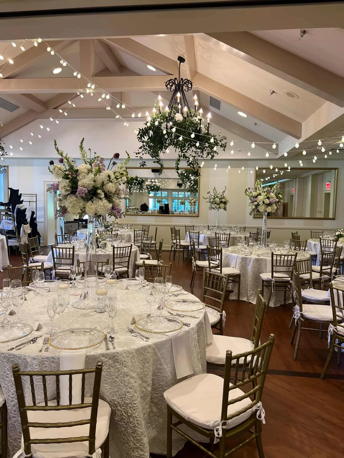 Elegant banquet hall decorated with floral centerpieces, string lights, and a large mirror on the wall.