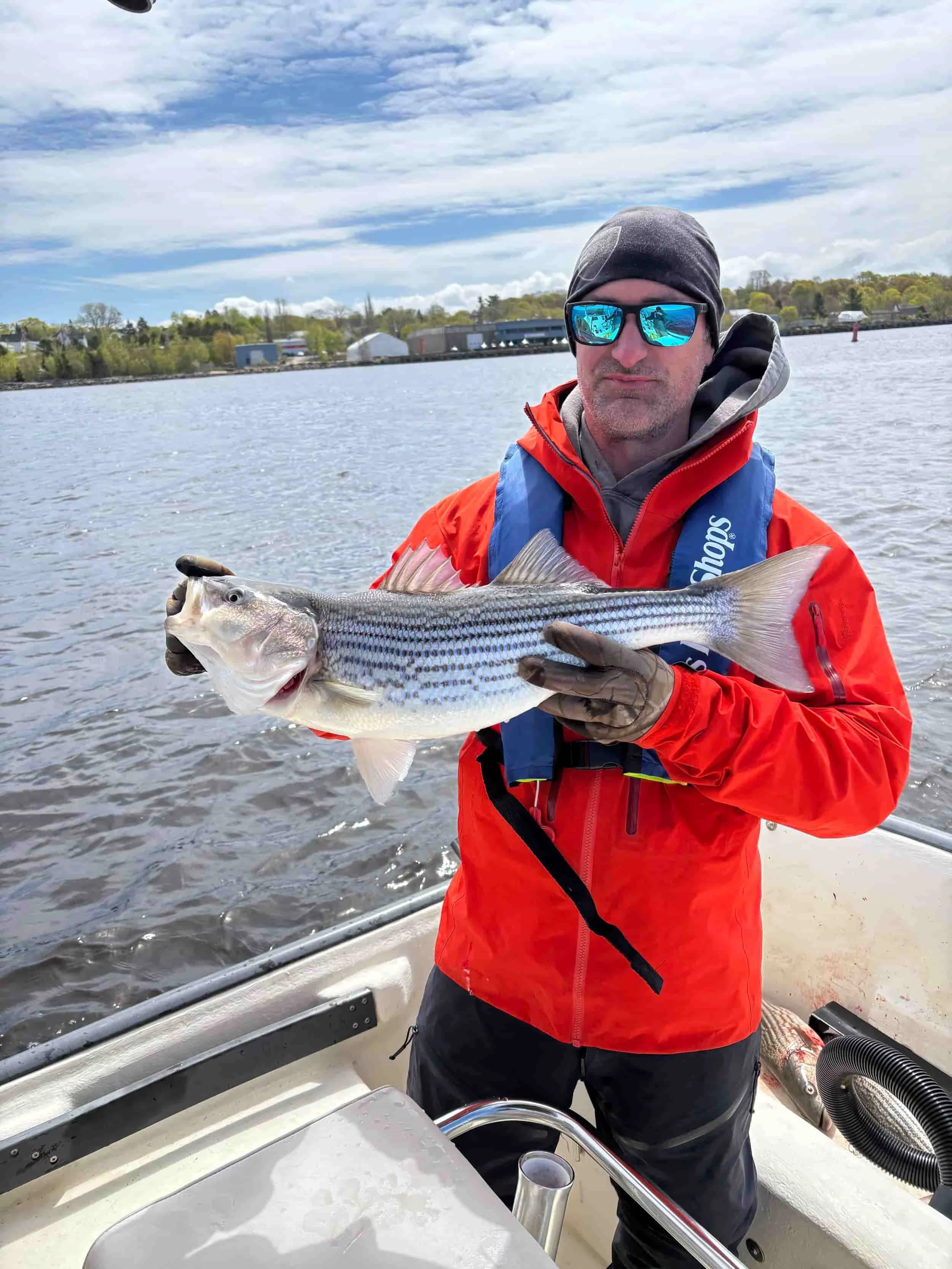 Man in red jacket and sunglasses holding a striped fish on boat water background.