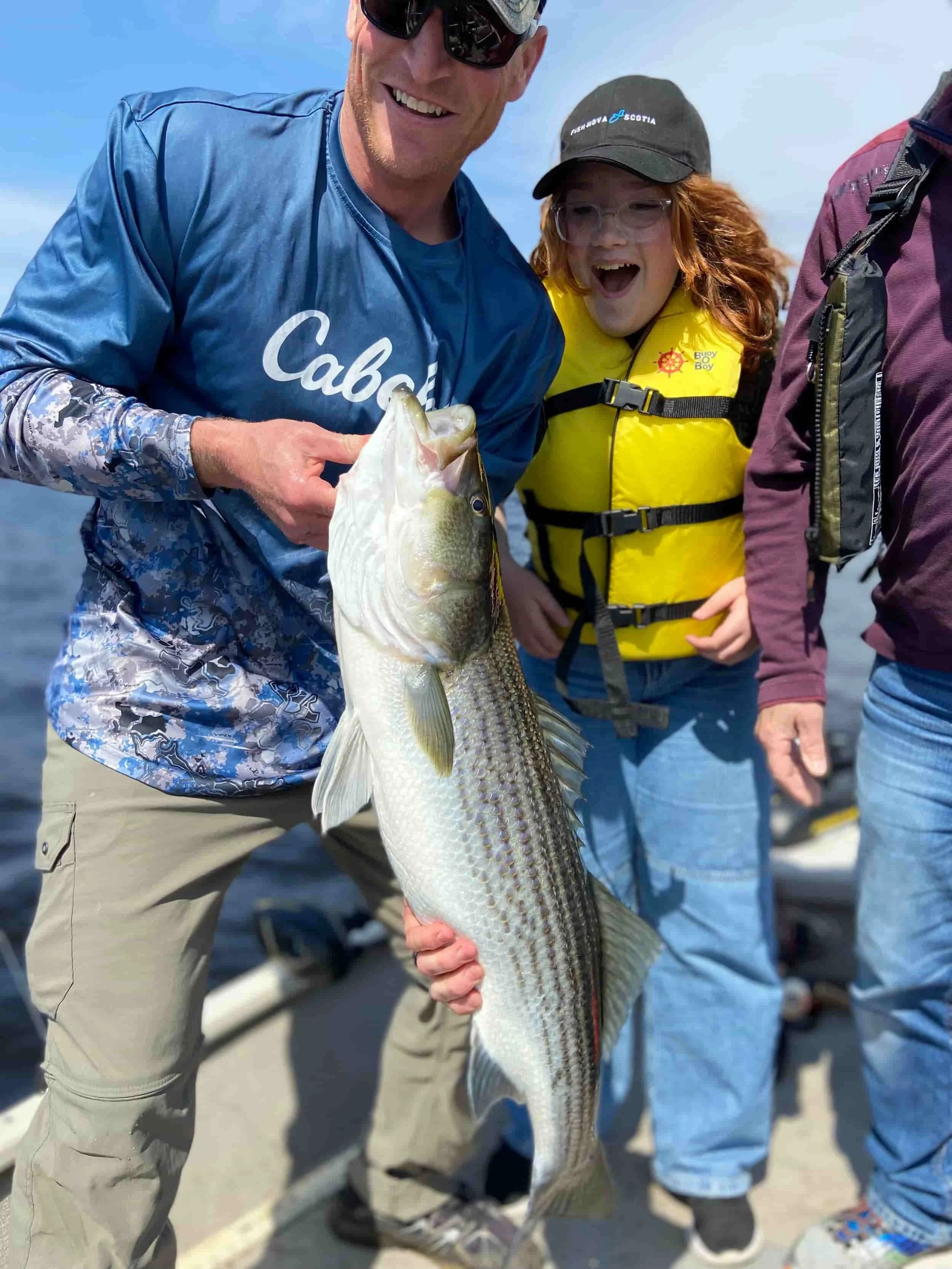 Group of people on a boat holding a large fish, with one person wearing a yellow life vest and smiling.