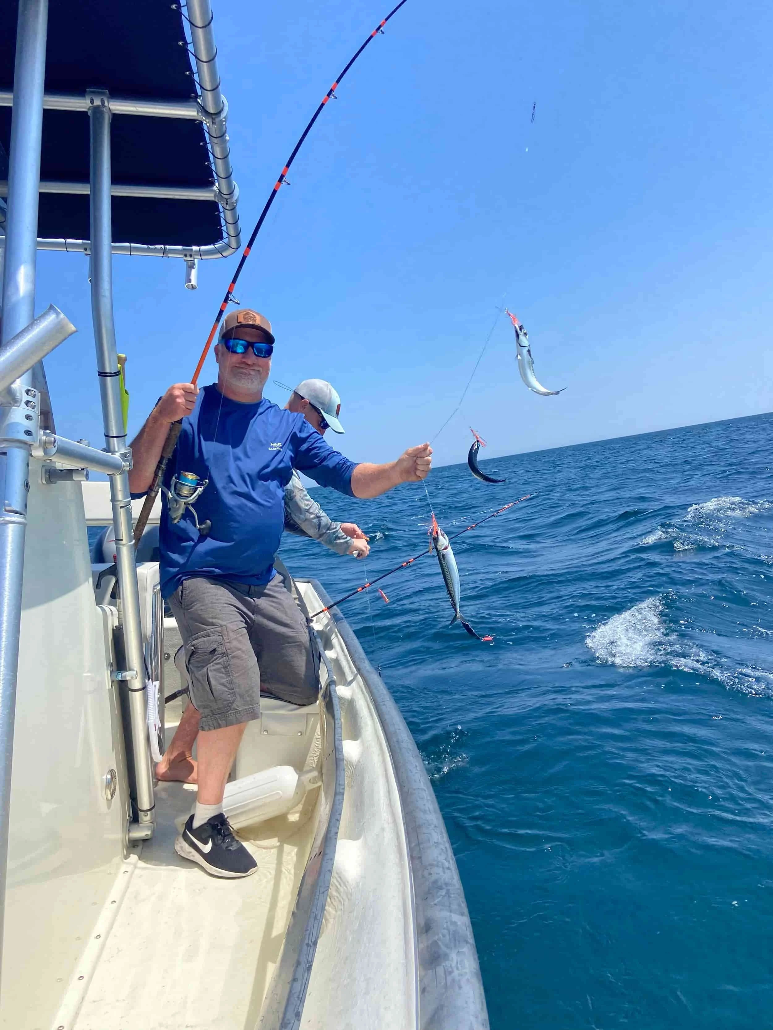 Man fishing on a boat in the ocean, holding a fishing rod with three fish caught and hanging from the line.