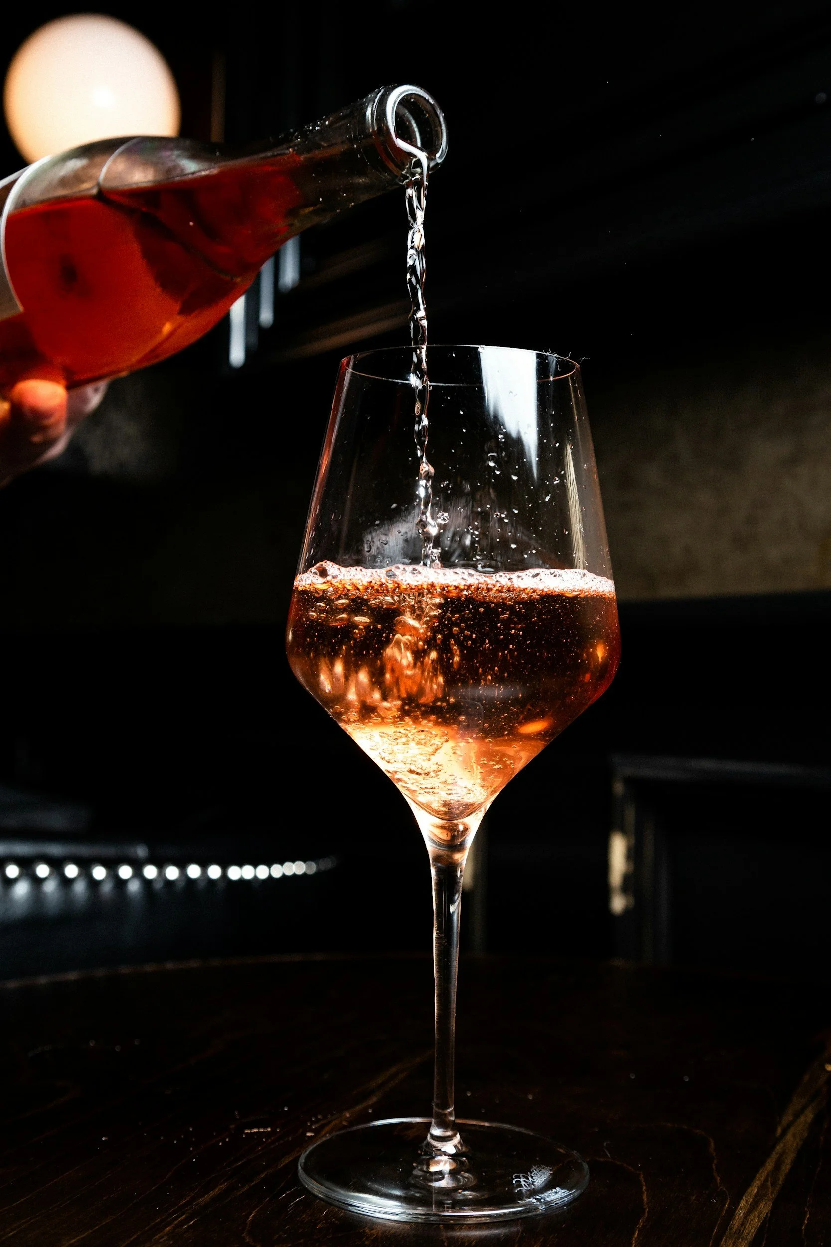 Rosé wine being poured into a glass on a dark wooden table.