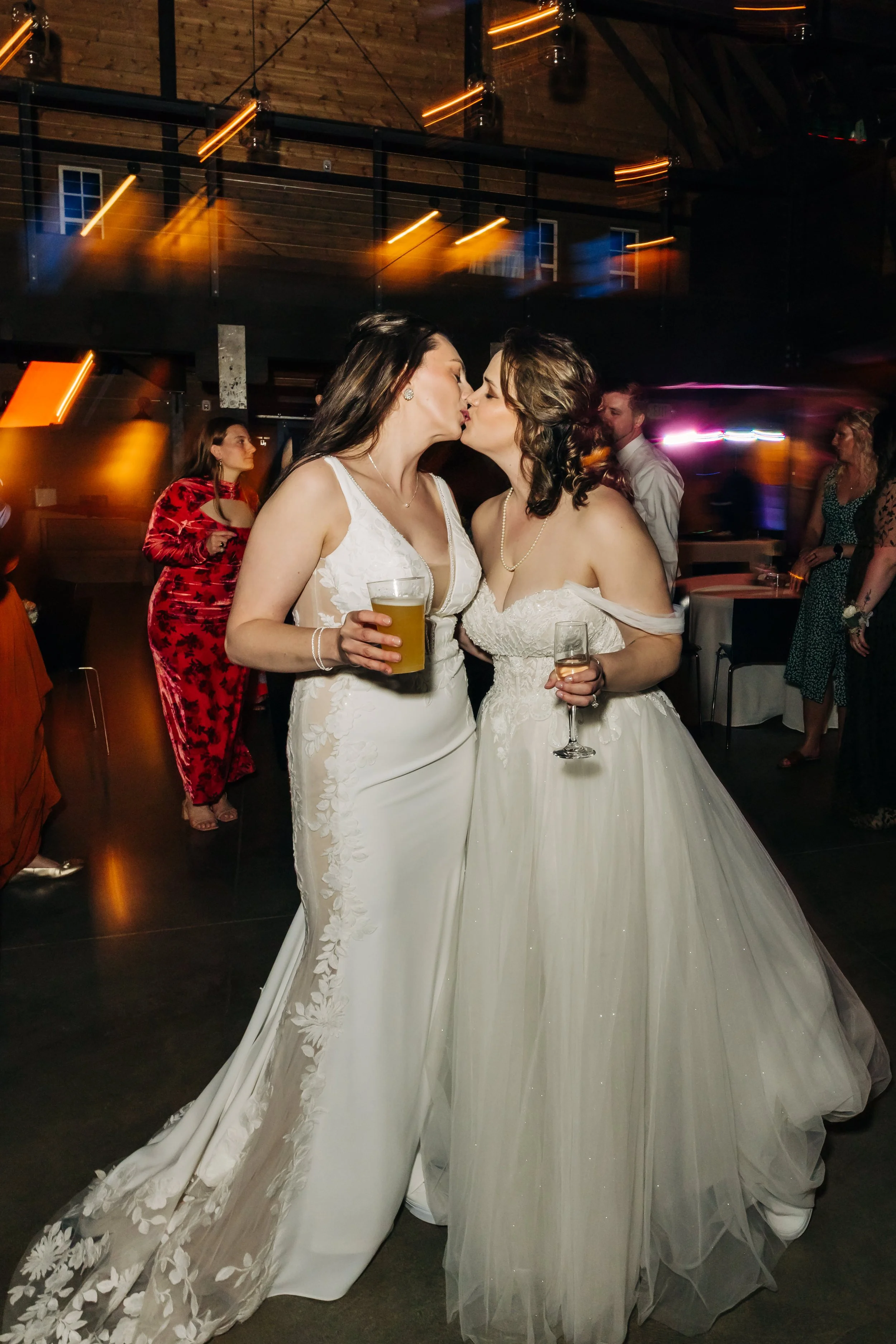 Two brides dressed in white wedding gowns sharing a kiss at a Marionfield farm wedding reception.