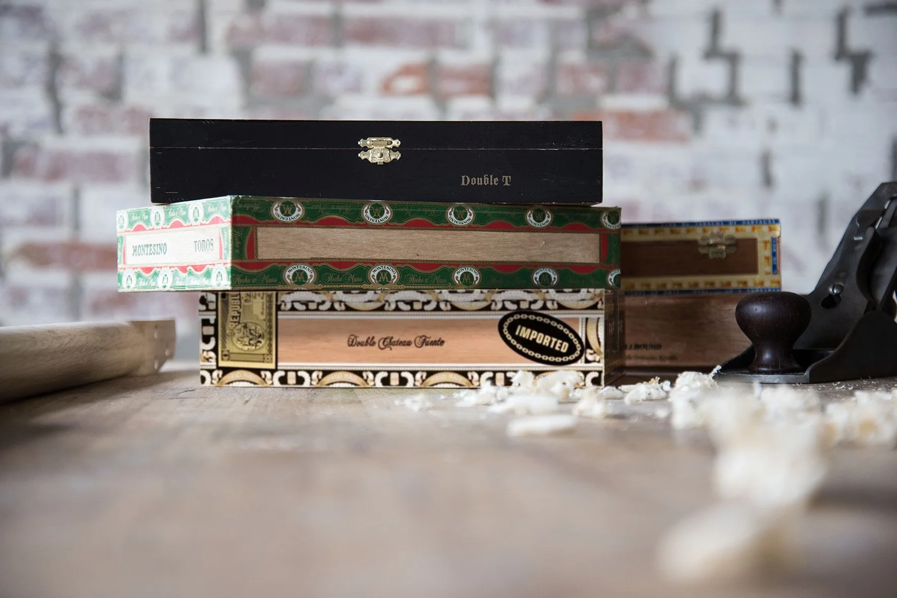 Stack of decorative cigar boxes on a wooden table with a blurred background; wood shavings and a hand planer nearby.
