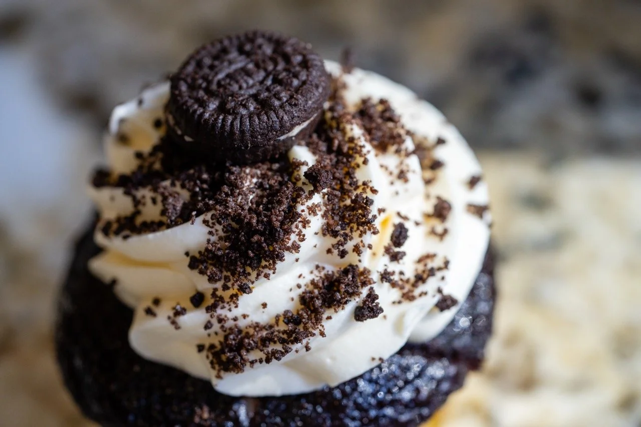 A chocolate cupcake topped with white frosting, a mini Oreo, and chocolate cookie crumbles