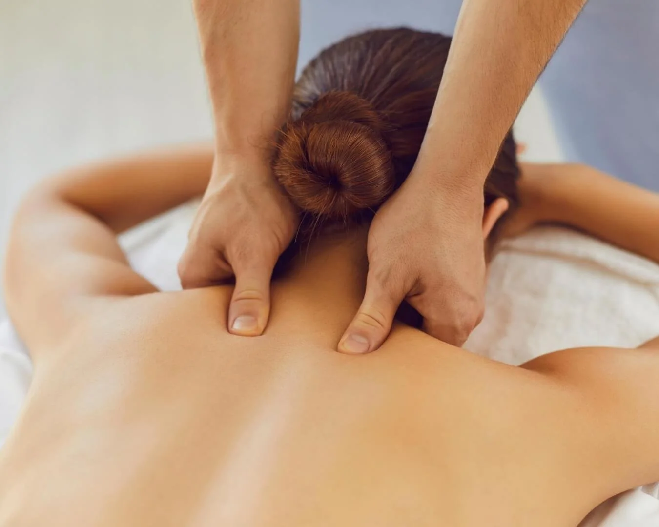 A person is receiving a massage with focused pressure on their upper back and shoulders.