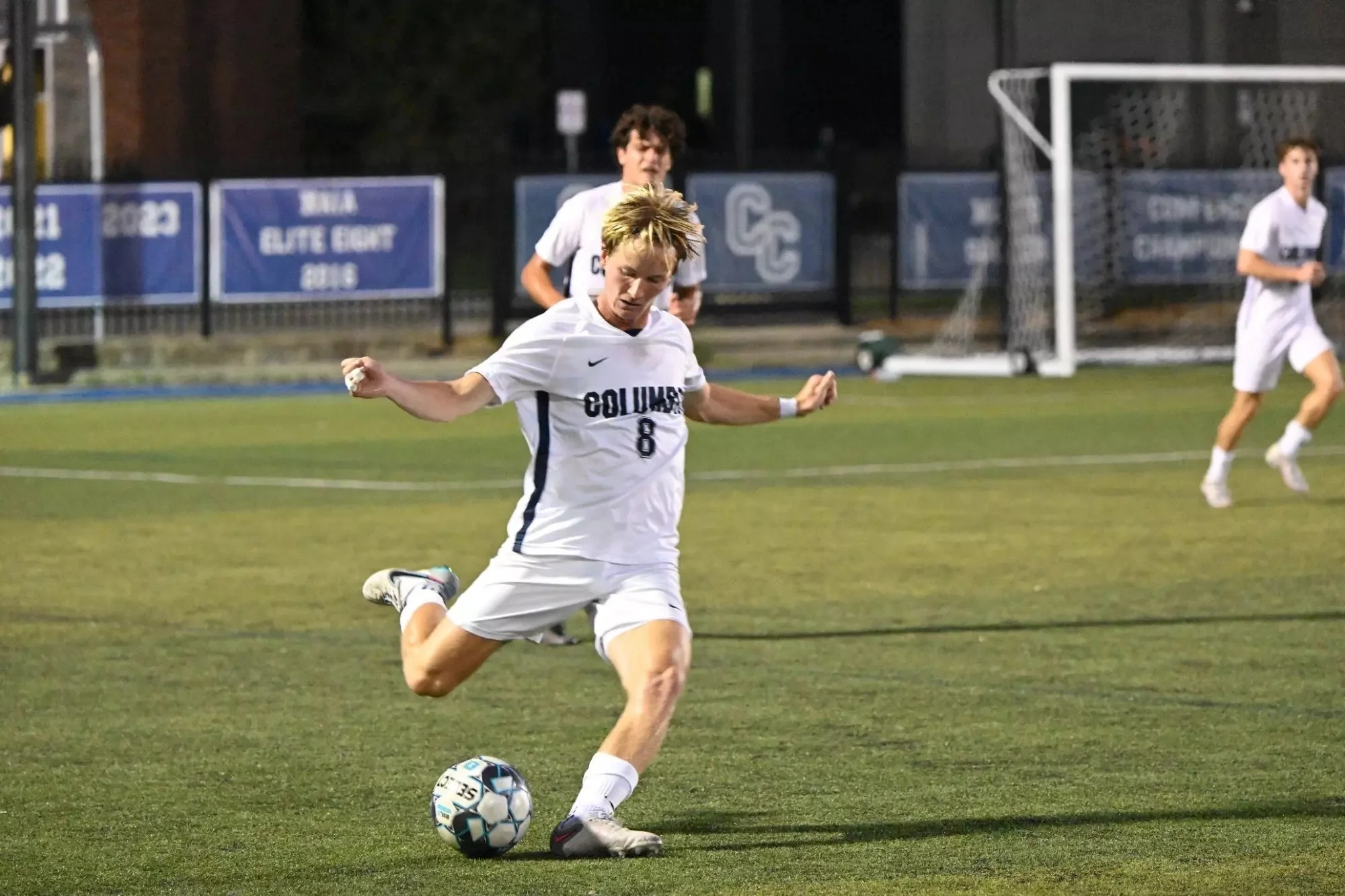Close-up of a young woman with short black hair smiling in a greenhouse with green plants in the background.