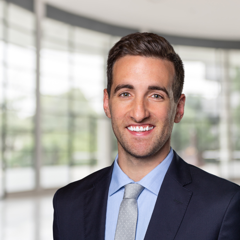 Professional young man in a suit smiling in a modern office with large windows and natural light.