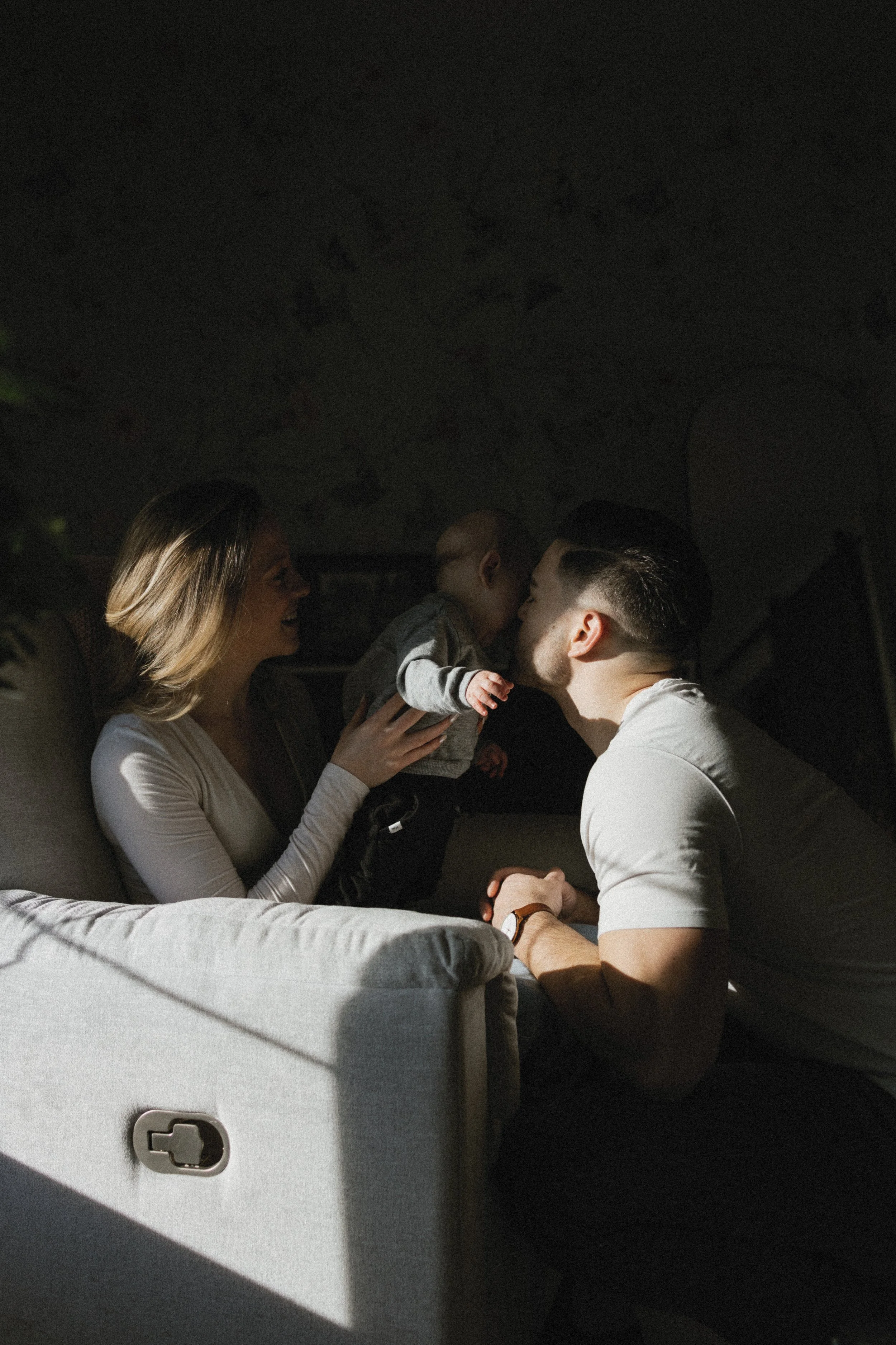 A family with a baby sitting on a couch in a dimly lit room.