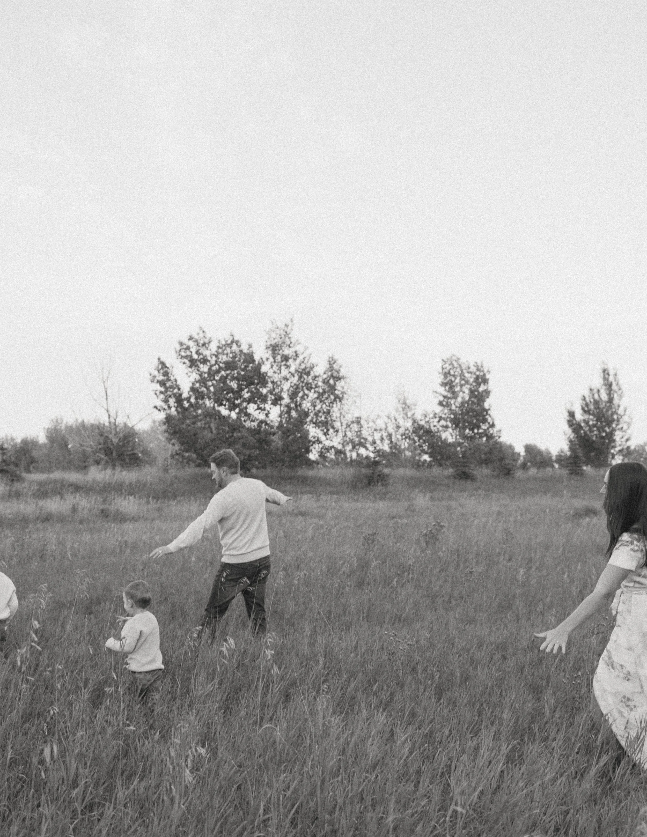 Black and white photo of a family playing in a grassy field, with trees in the background.