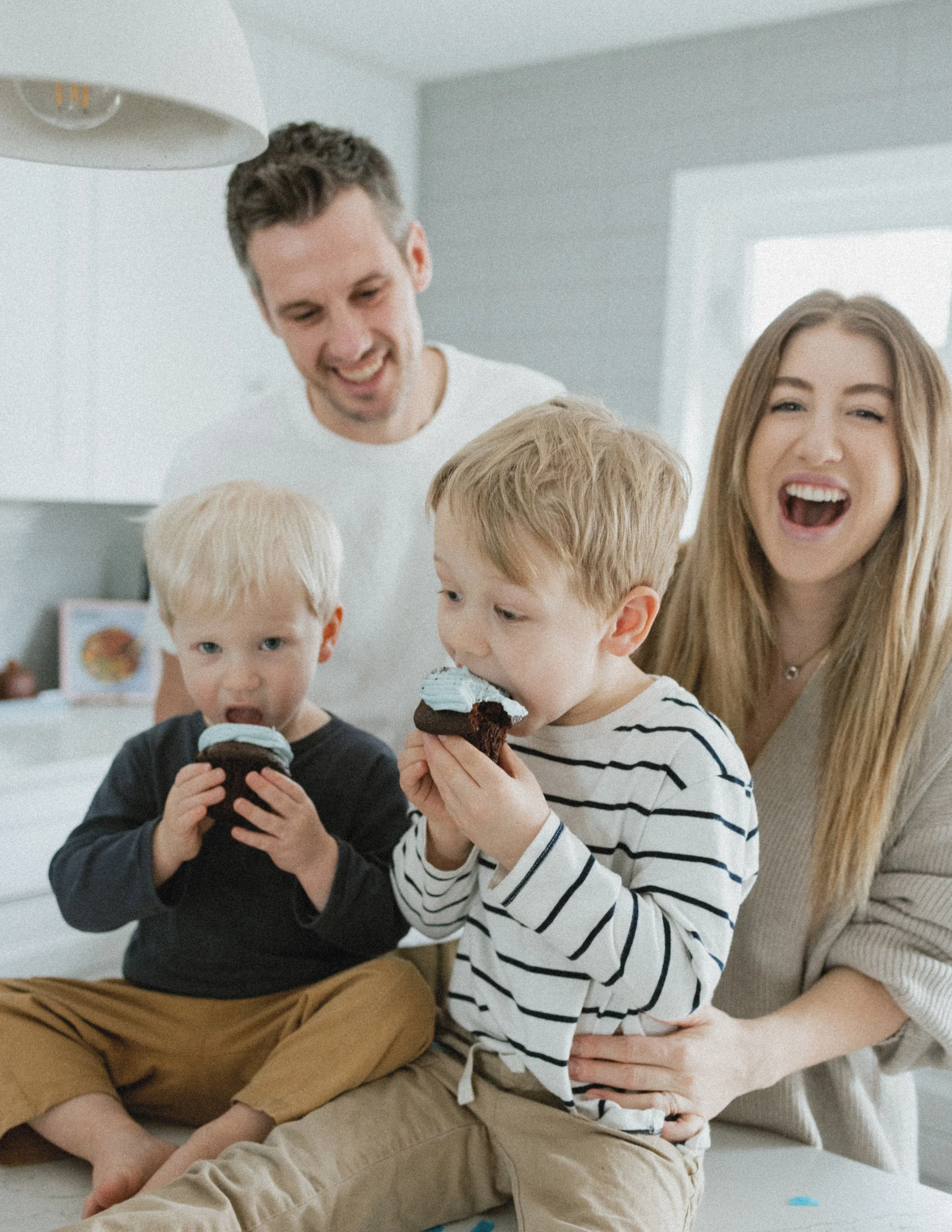Family in kitchen with two young children eating cupcakes.