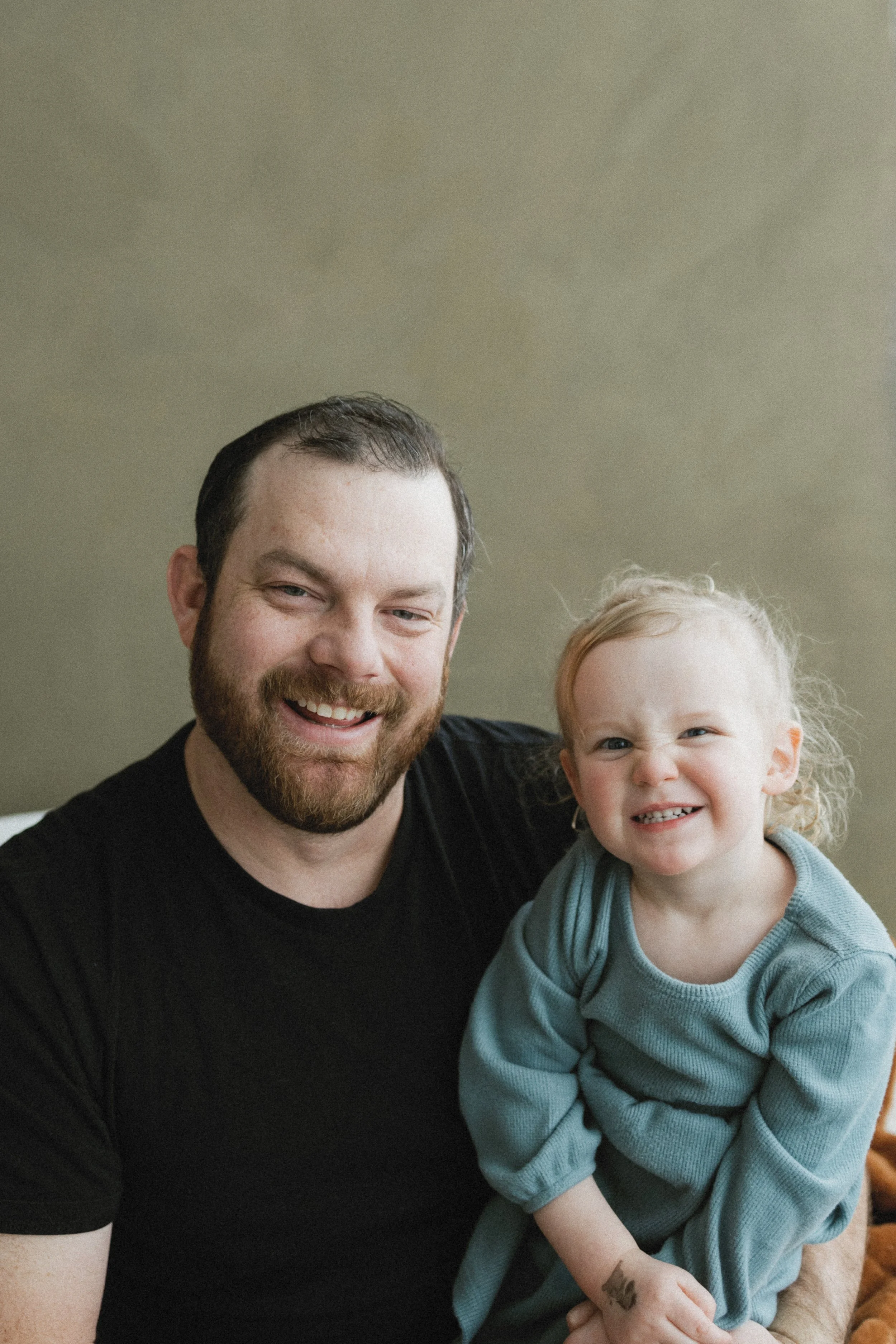 Man and child smiling, both wearing blue clothing, neutral background