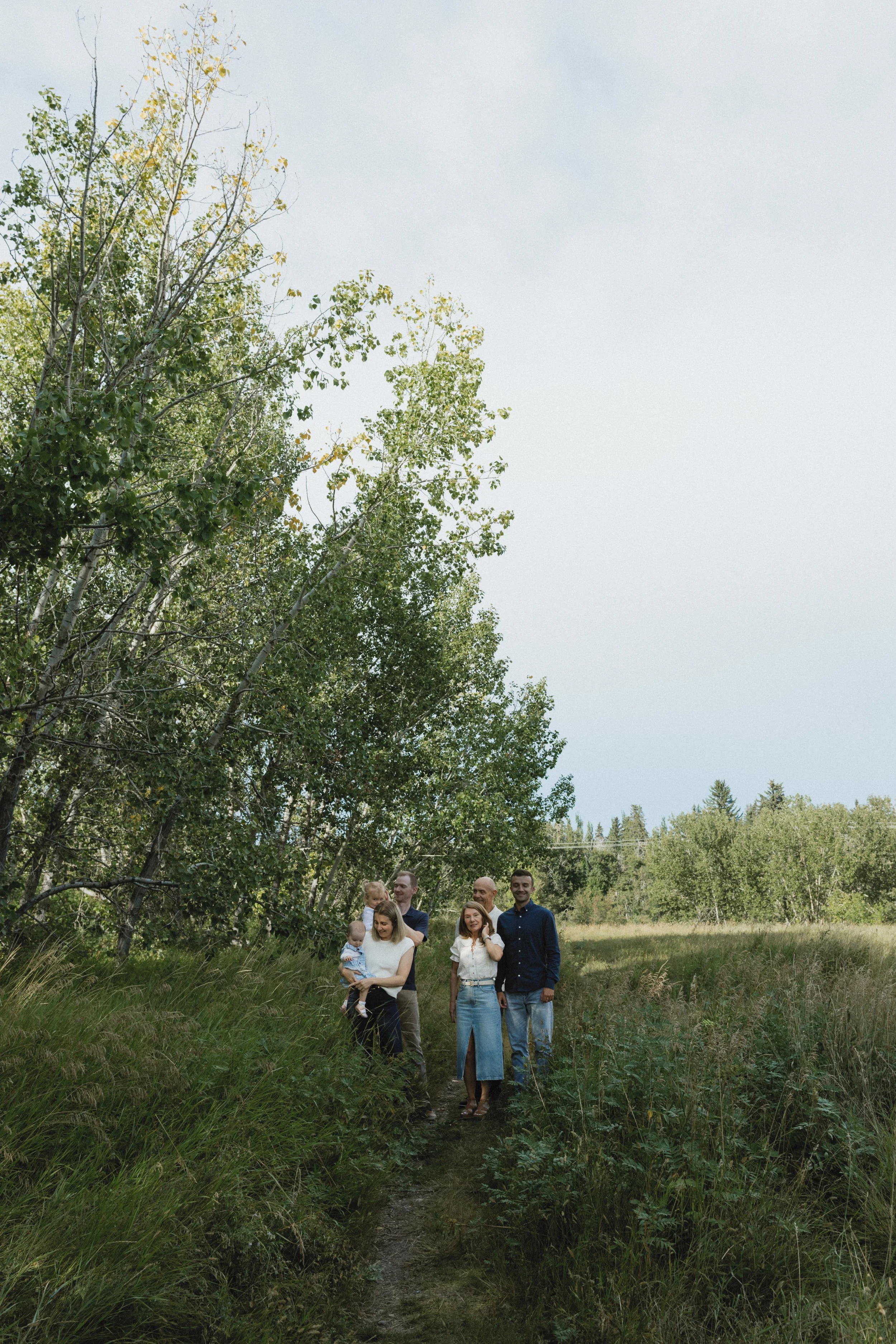 Family walking on a path in a grassy field with tall trees in the background.