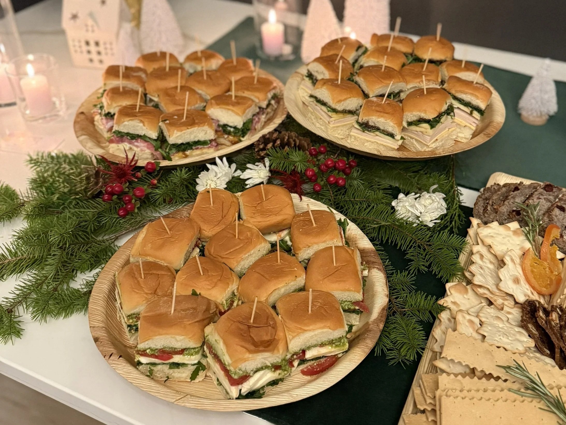 Assorted sandwiches on wooden trays, decorated with greenery and berries, served on a table with Christmas decorations.