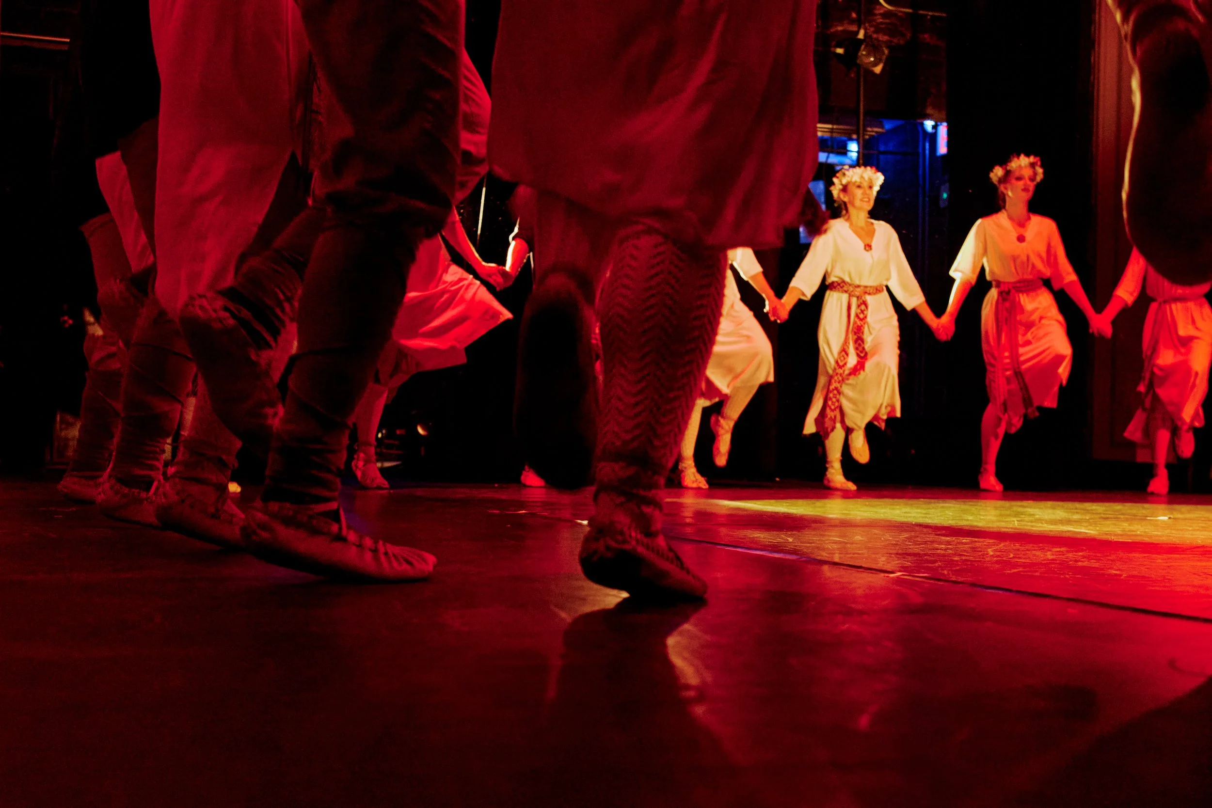 People dancing in traditional clothing holding hands on stage, viewed from a low angle.