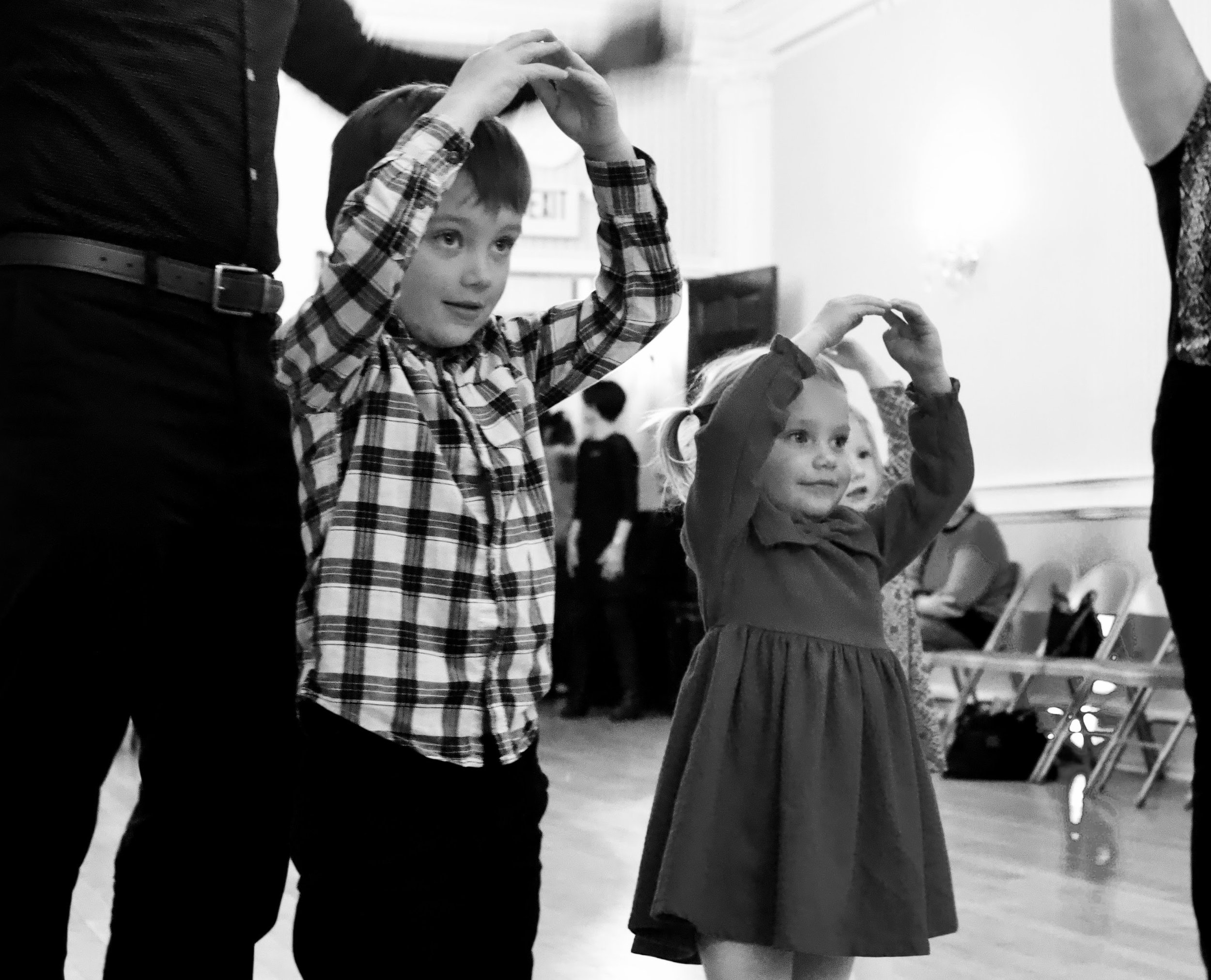 Children at an indoor event, holding hands above their heads, participating in a group activity.