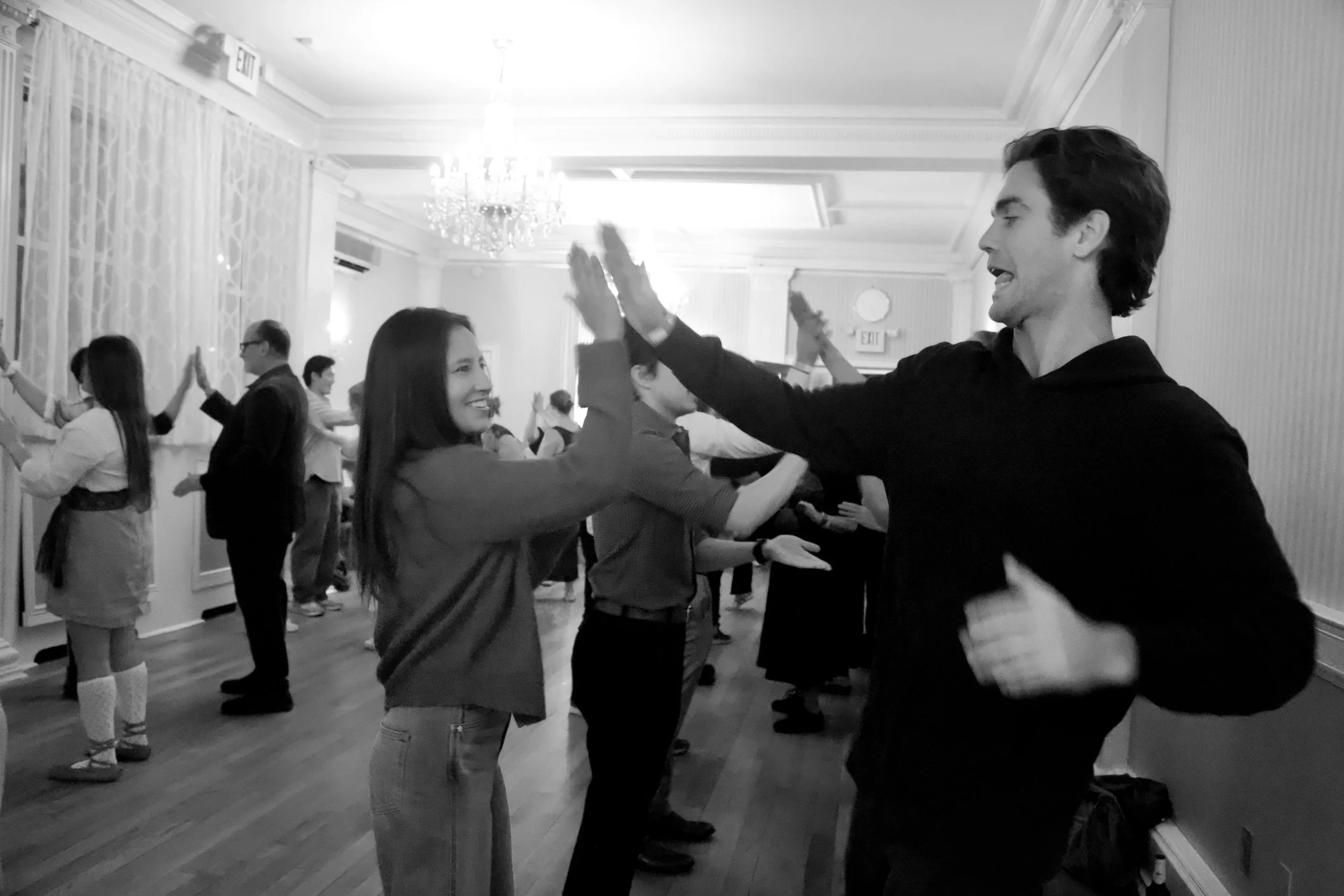 People dancing and high-fiving at a social event in a decorated ballroom with chandeliers.