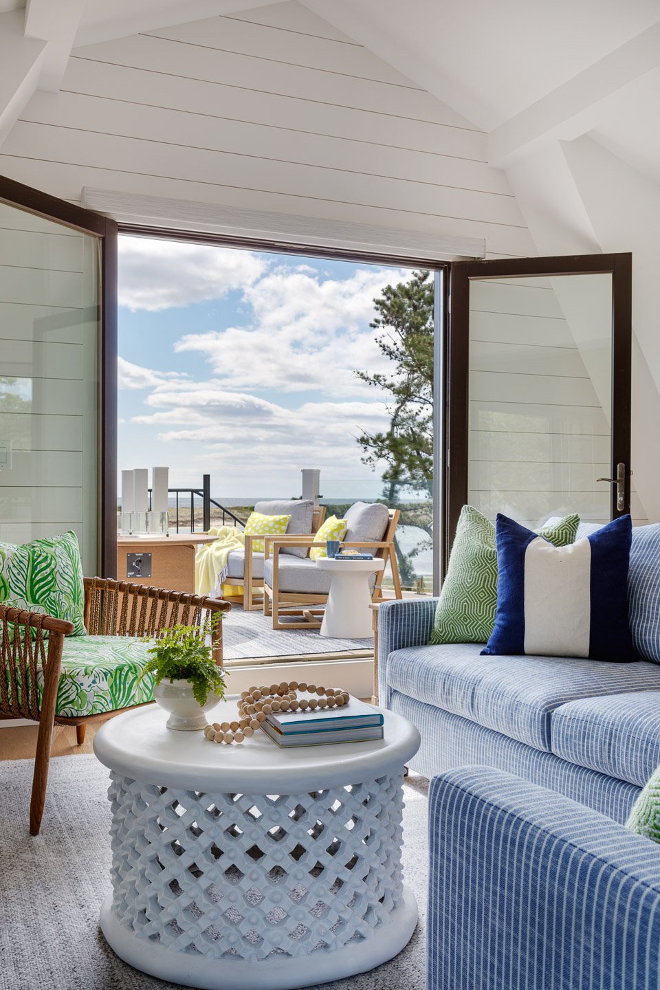 A bright and inviting coastal lounge designed by Lindsey Architects, featuring vaulted ceilings, expansive folding glass doors, and seamless indoor-outdoor living overlooking the Maine coastline. Soft coastal-inspired furnishings, natural textures, a