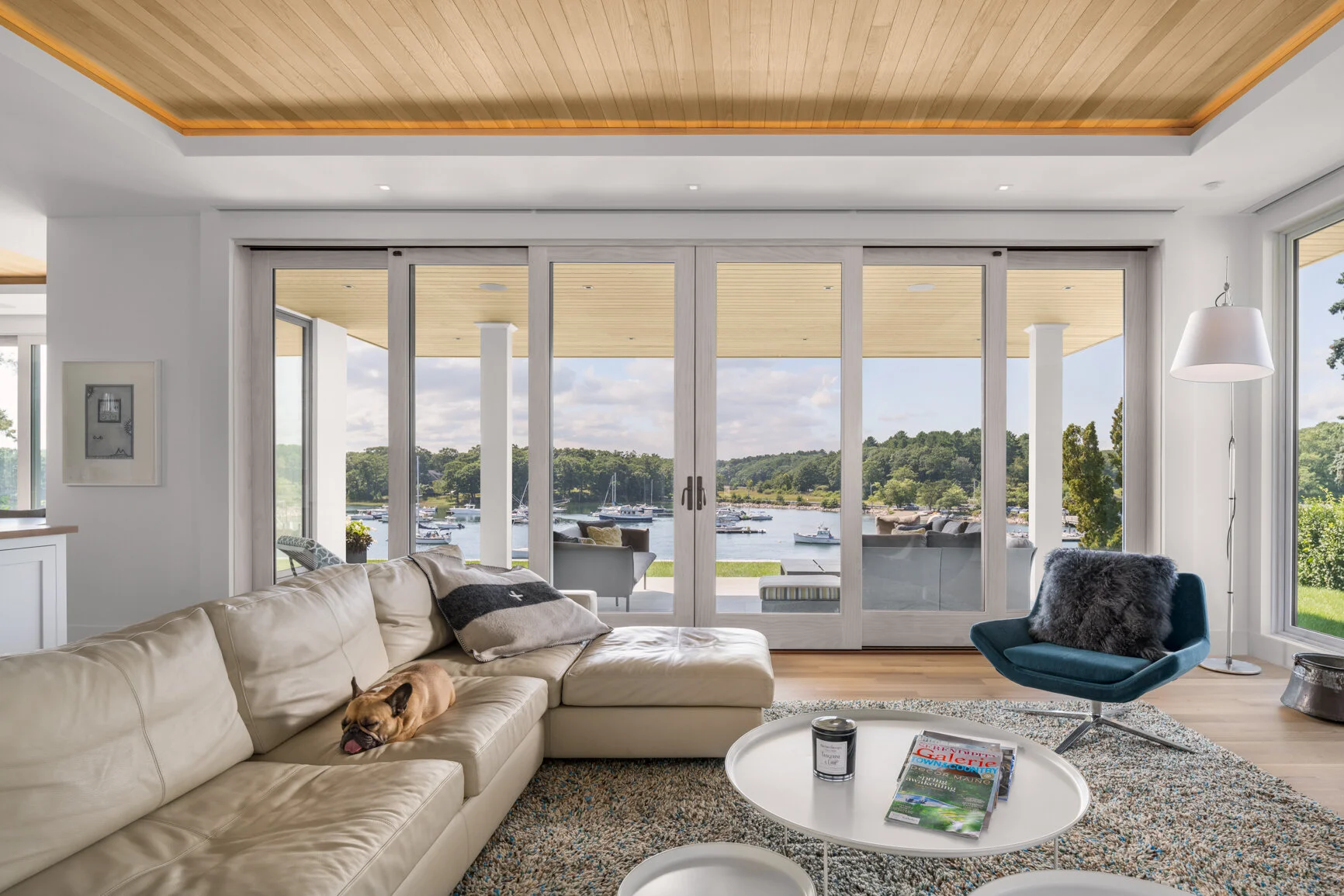 A contemporary waterfront living space designed by Lindsey Architects, blending expansive glass walls, warm natural wood ceilings, and refined modern detailing to create a seamless connection to the surrounding coastal landscape. Framed water views, 