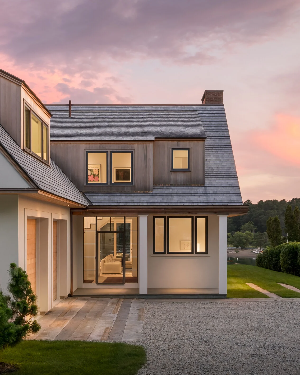 A refined evening view of a custom coastal residence designed by Lindsey Architects, blending contemporary New England architecture with warm natural materials and carefully detailed modern forms. Soft interior lighting, expansive glass openings, and